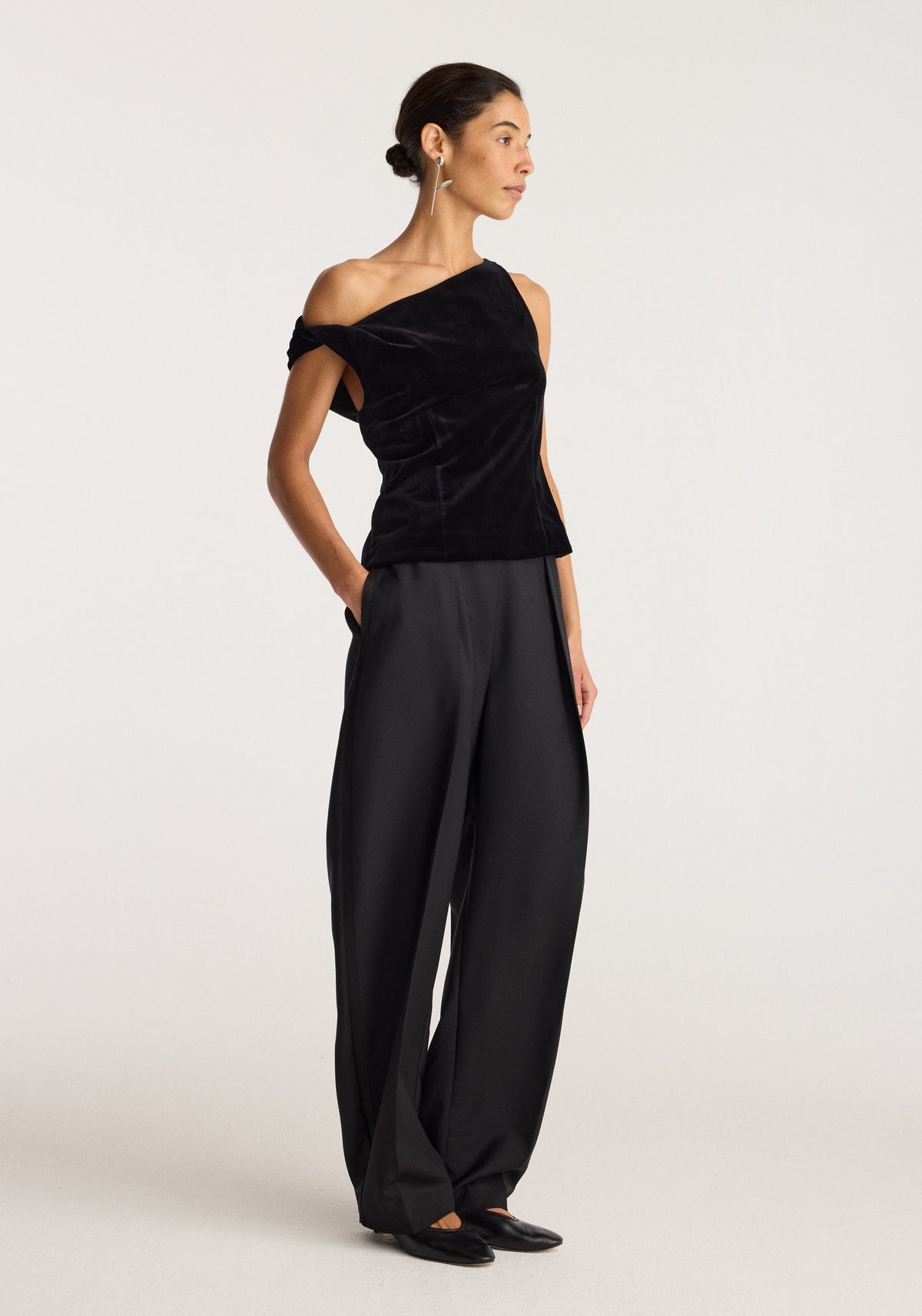 Draped velvet top | black with an asymmetrical neckline and gathered draping worn with wide leg trousers by a model in a studio setting