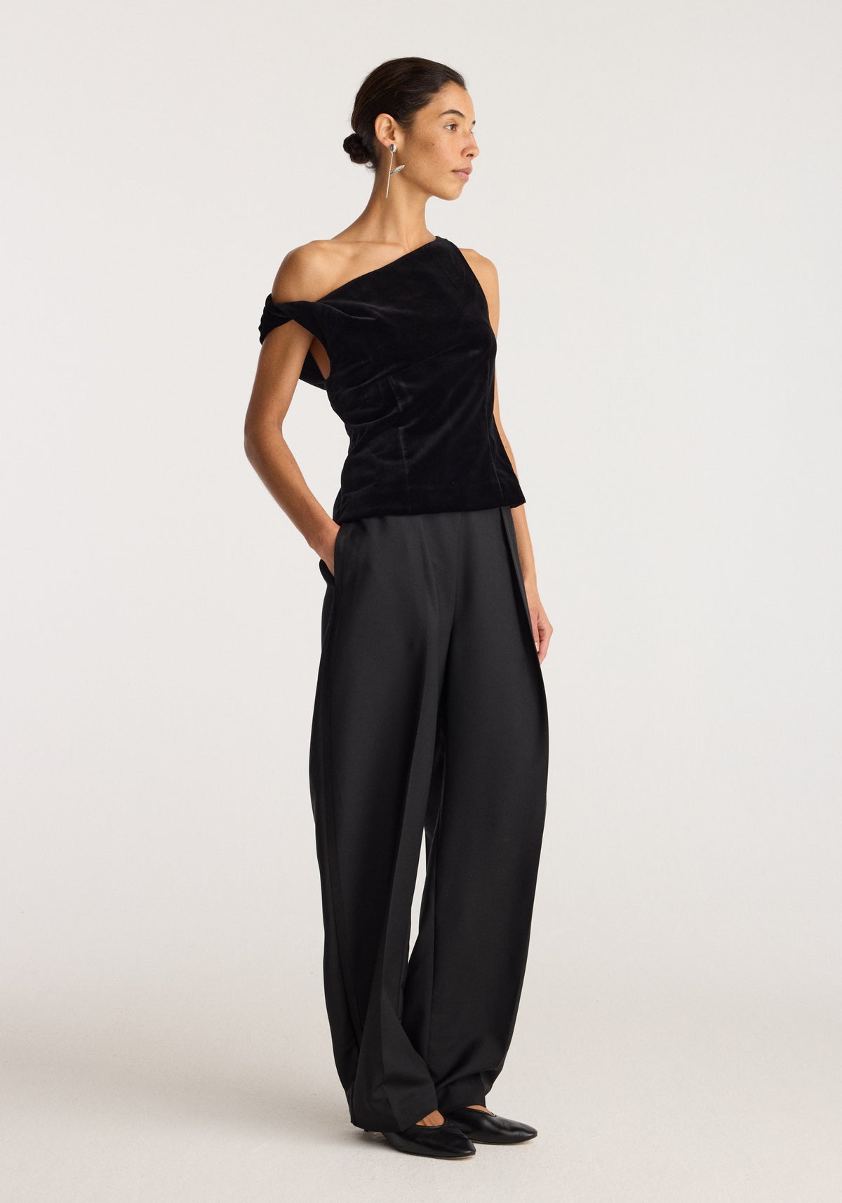 Draped velvet top | black worn by a model with wide leg trousers and pointed flats in a light studio setting