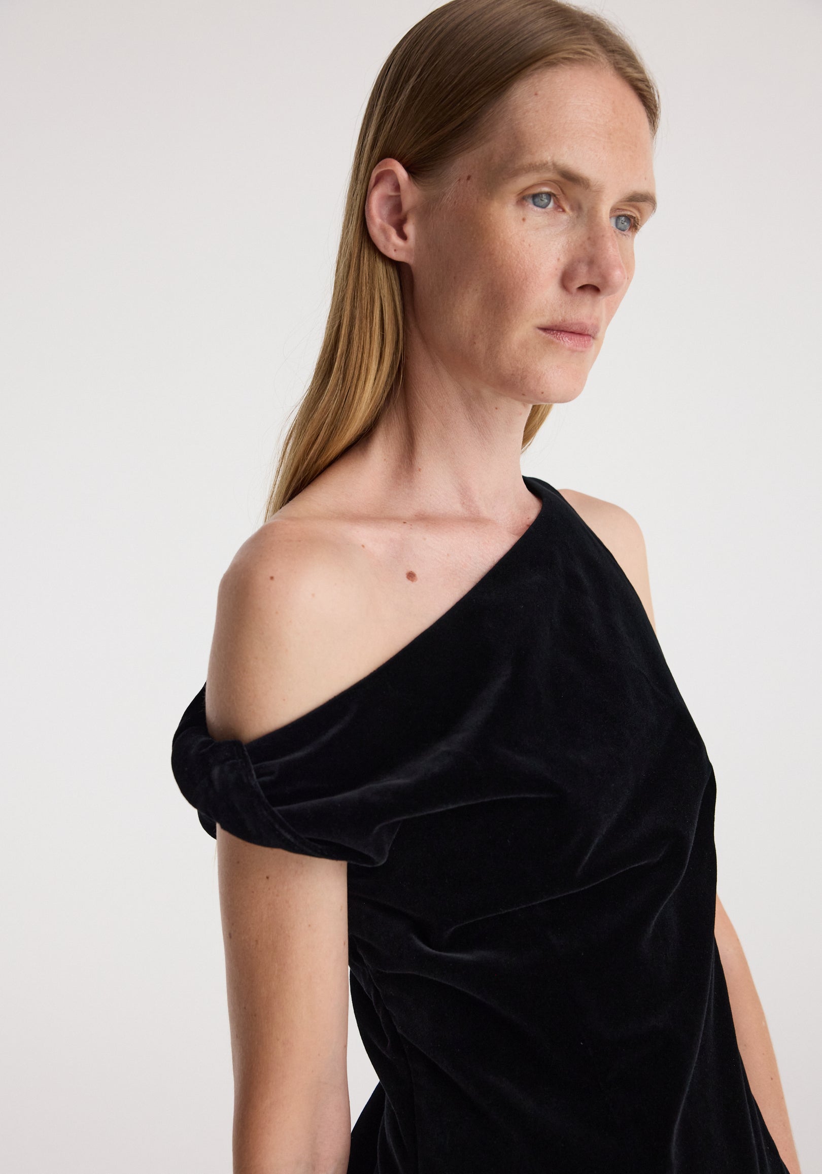 Woman wearing a draped velvet top | black with an off-the-shoulder design, showcasing the soft texture and elegant draping of the fabric.