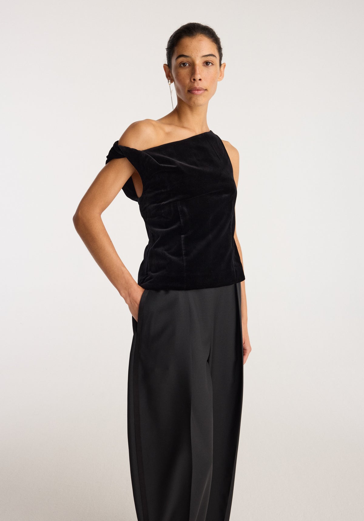 Draped velvet top | black shown on a model with an asymmetrical one shoulder neckline and soft draping styled with wide leg black trousers