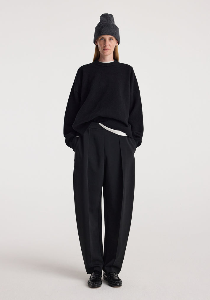Person wearing a Beanie | anthracite melange styled with a black oversized sweater, black pleated trousers, and black shoes against a plain white background.