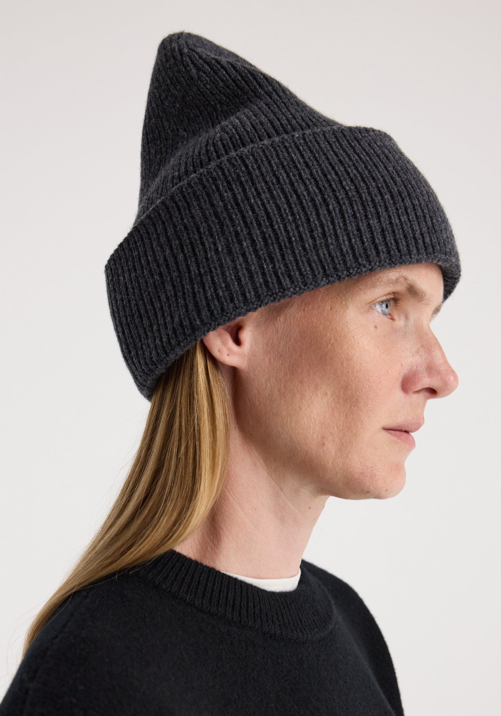 Side profile of a person wearing a dark grey knitted hat with a folded brim and pointed top, styled with a black sweater, featuring the Beanie | anthracite melange.