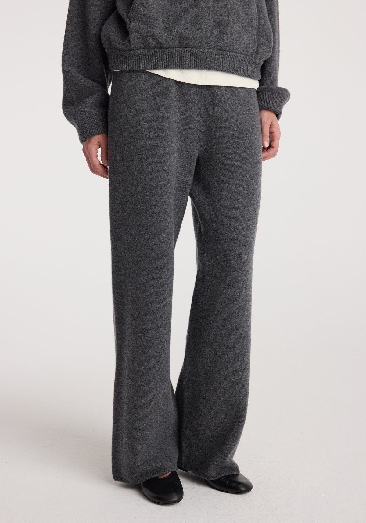 Close-up of a person wearing Compact knitted trousers | dark grey melange featuring a relaxed fit and soft texture paired with black shoes against a plain background.