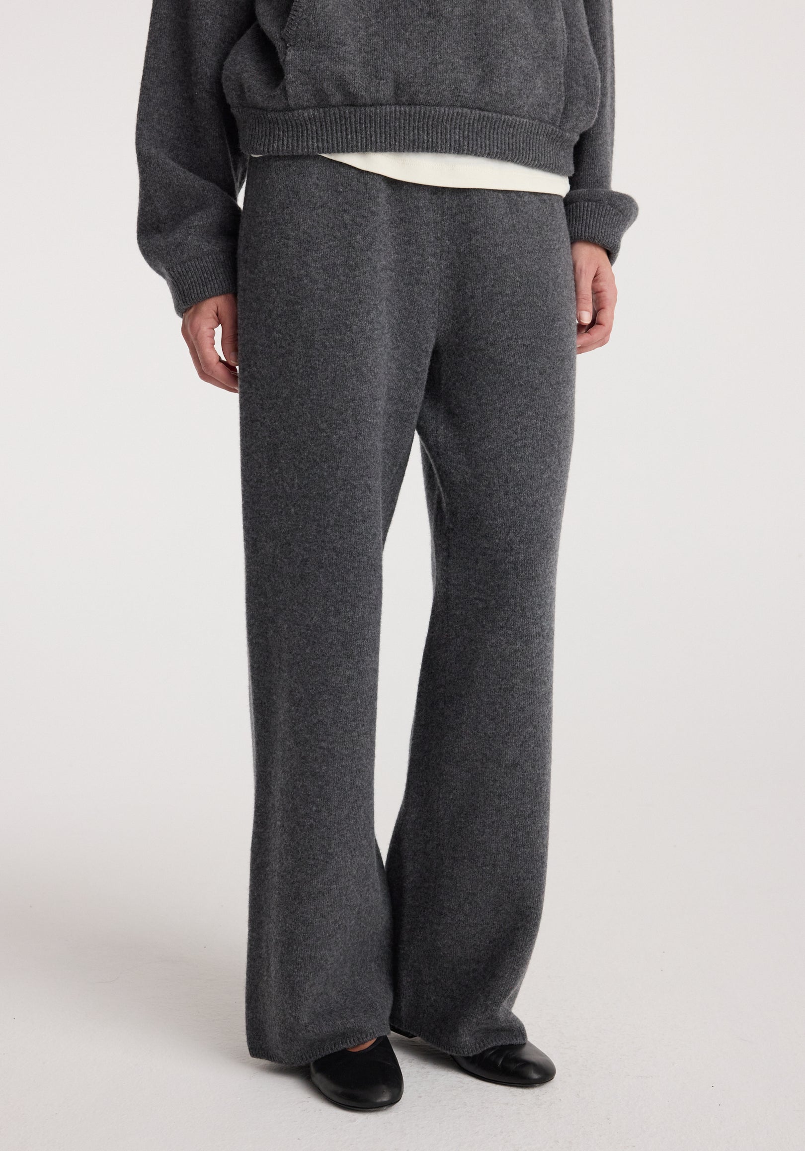 Close-up of a person wearing Compact knitted trousers | dark grey melange featuring a relaxed fit and soft texture paired with black shoes against a plain background.