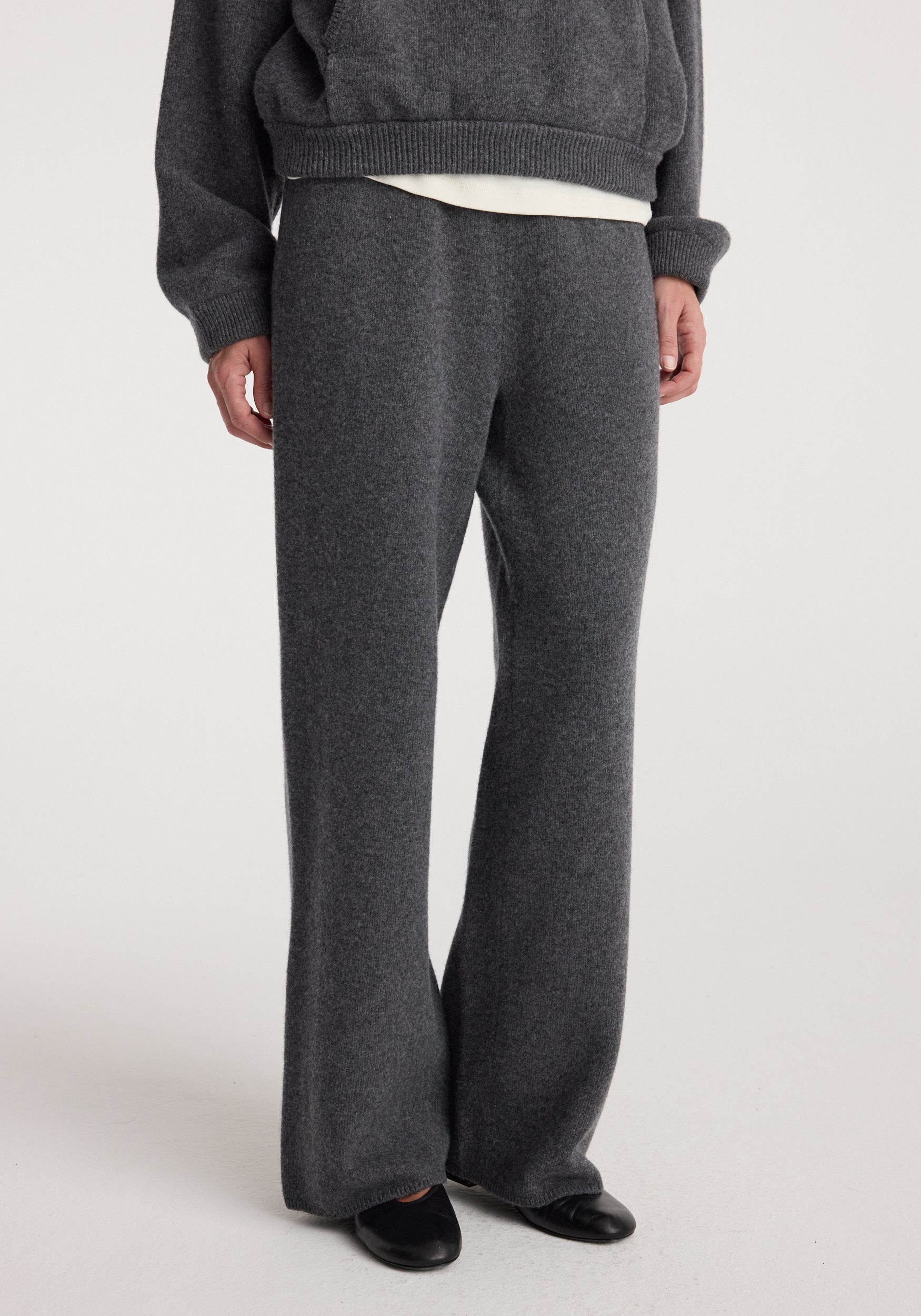 Close-up of a person wearing Compact knitted trousers | dark grey melange featuring a relaxed fit and soft texture paired with black shoes against a plain background.