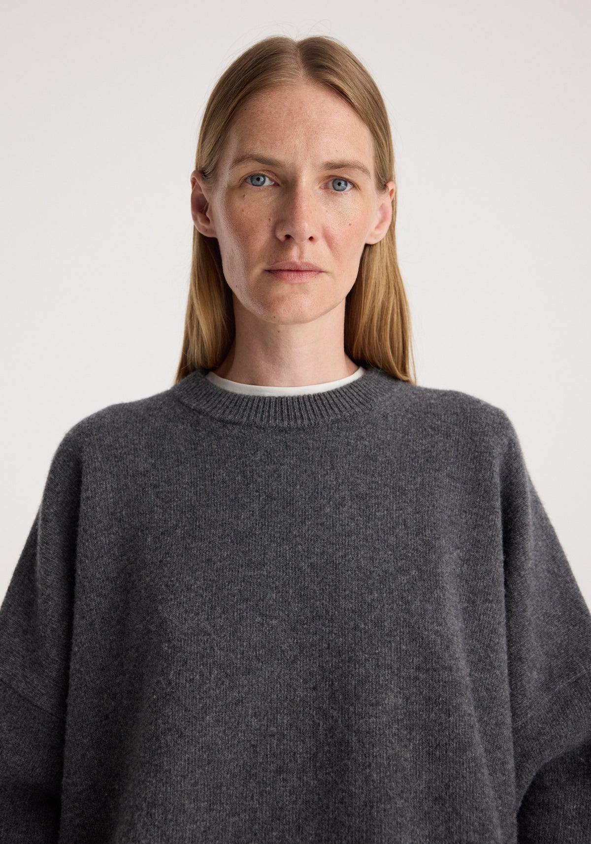Close-up of a woman wearing a Classic crewneck jumper | dark grey melange with a soft, textured fabric and a relaxed fit, featuring a ribbed neckline over a white undershirt.