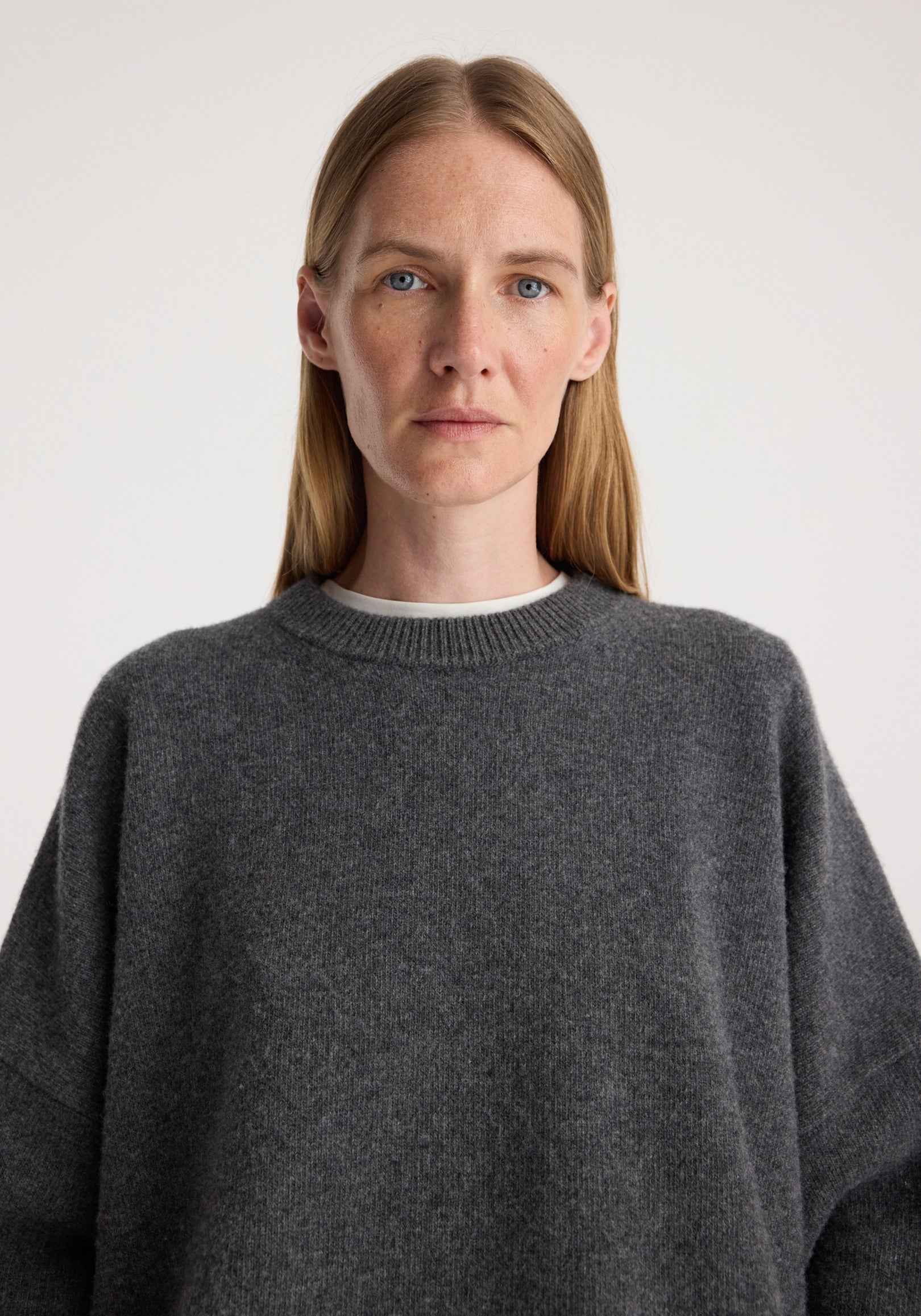 Close-up of a woman wearing a Classic crewneck jumper | dark grey melange with a soft, textured fabric and a relaxed fit, featuring a ribbed neckline over a white undershirt.