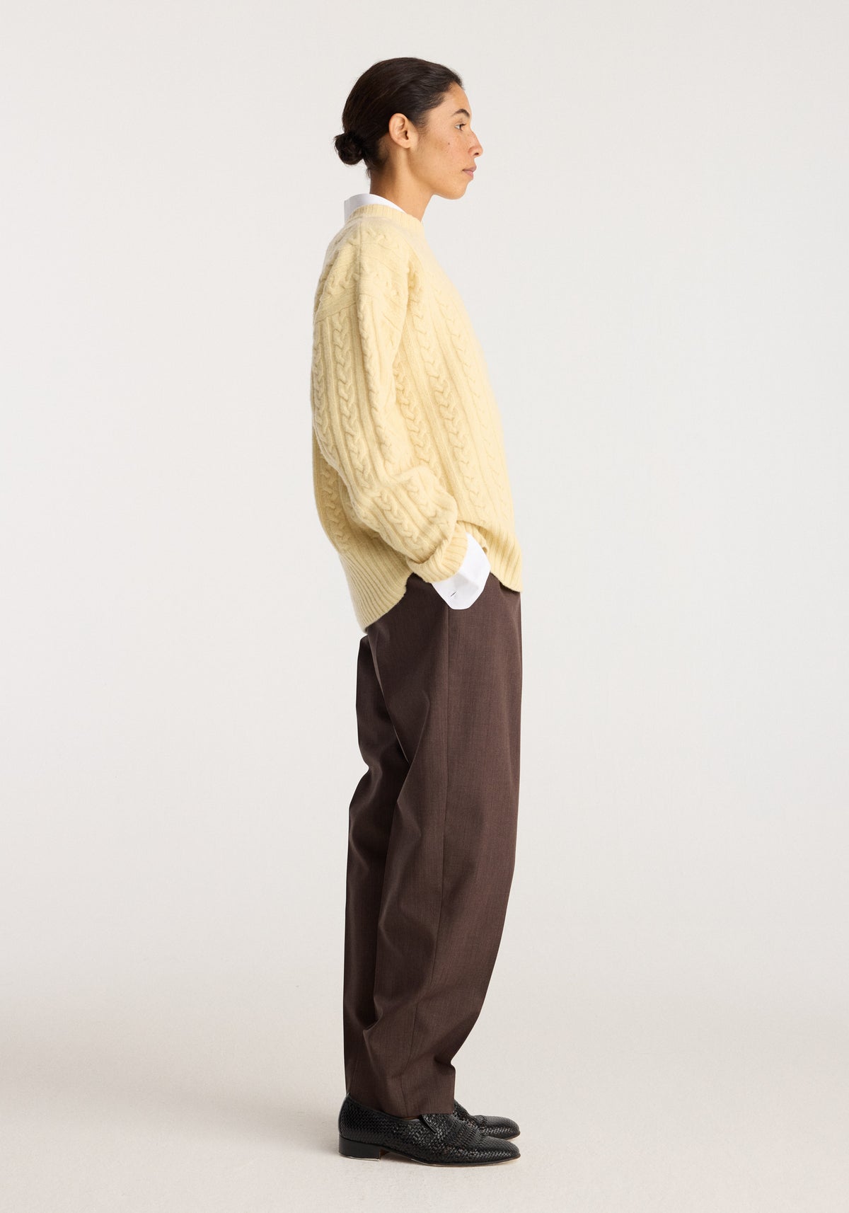 Cable knit jumper | butter worn in side profile by a model with cable knit texture and relaxed sleeves styled with brown trousers and black shoes