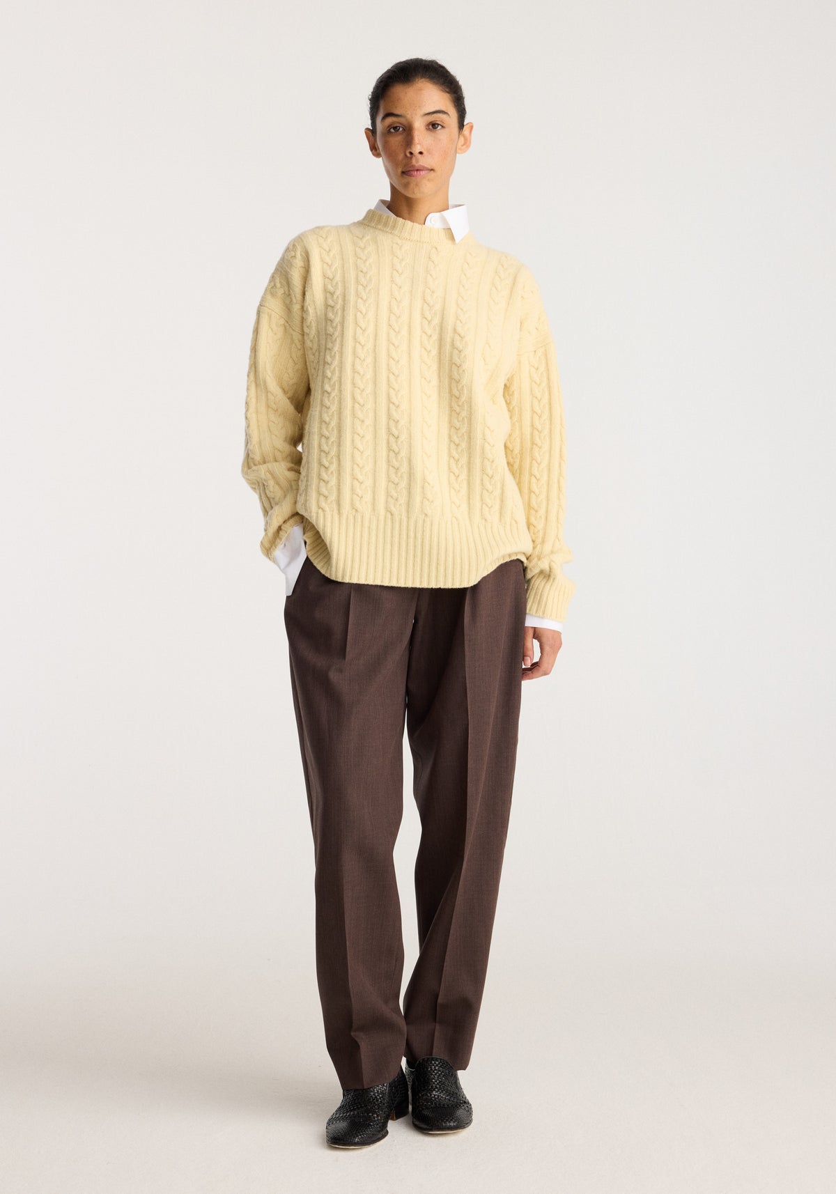 Cable knit jumper | butter worn by a model, featuring a cream cable knit design with ribbed trims, paired with brown trousers and black shoes