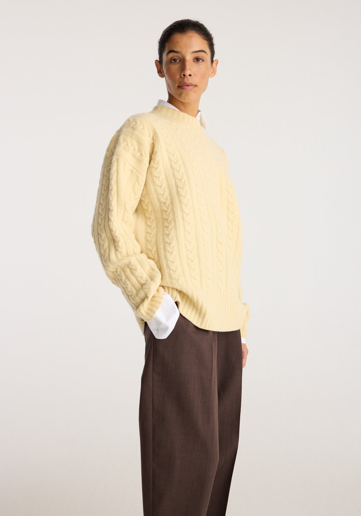 Cable knit jumper | butter worn by a model with a textured cable knit design long sleeves and a relaxed fit styled with brown trousers against a neutral backdrop