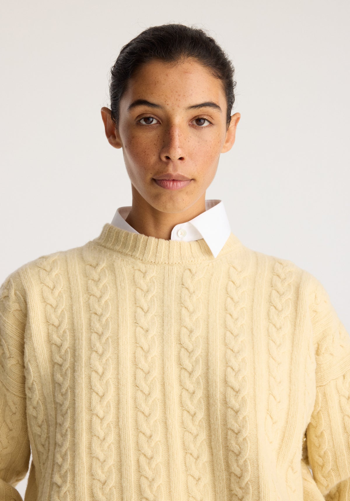 Cable knit jumper | butter worn over a white collared shirt, featuring a soft cream colour and textured vertical cable knit detailing