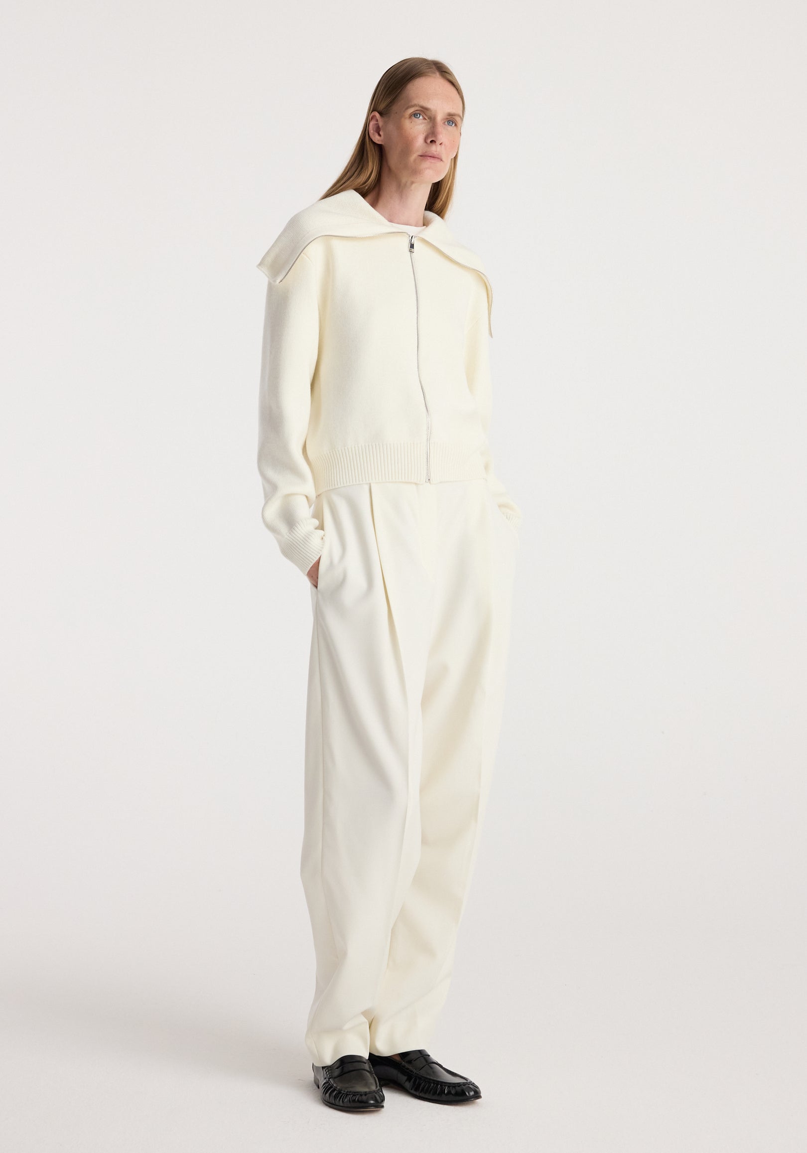 Woman wearing a cream Two way sailor zip cardigan | cream with long sleeves and a wide sailor collar, paired with matching cream wide-leg pants and black shoes, standing against a white background.
