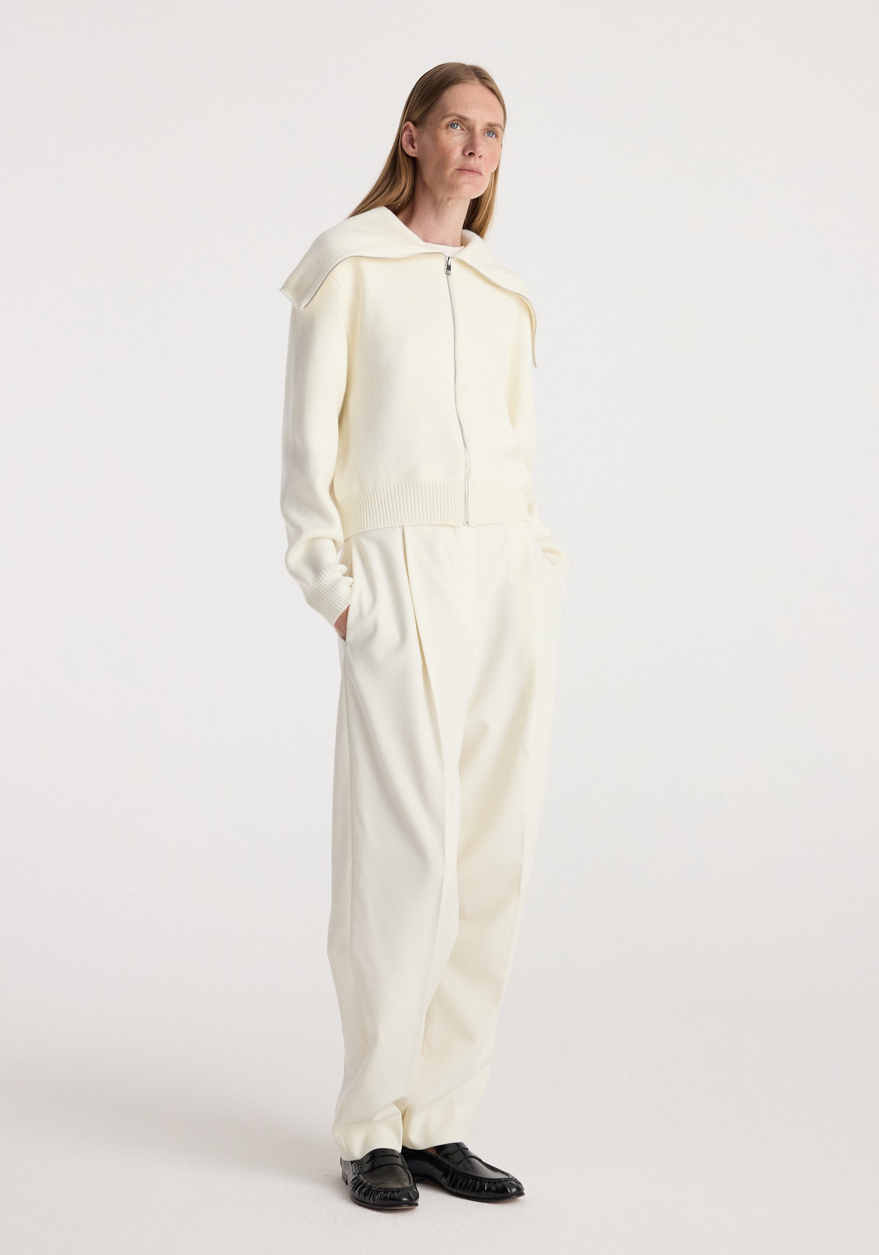 Woman wearing a cream Two way sailor zip cardigan | cream with long sleeves and a wide sailor collar, paired with matching cream wide-leg pants and black shoes, standing against a white background.