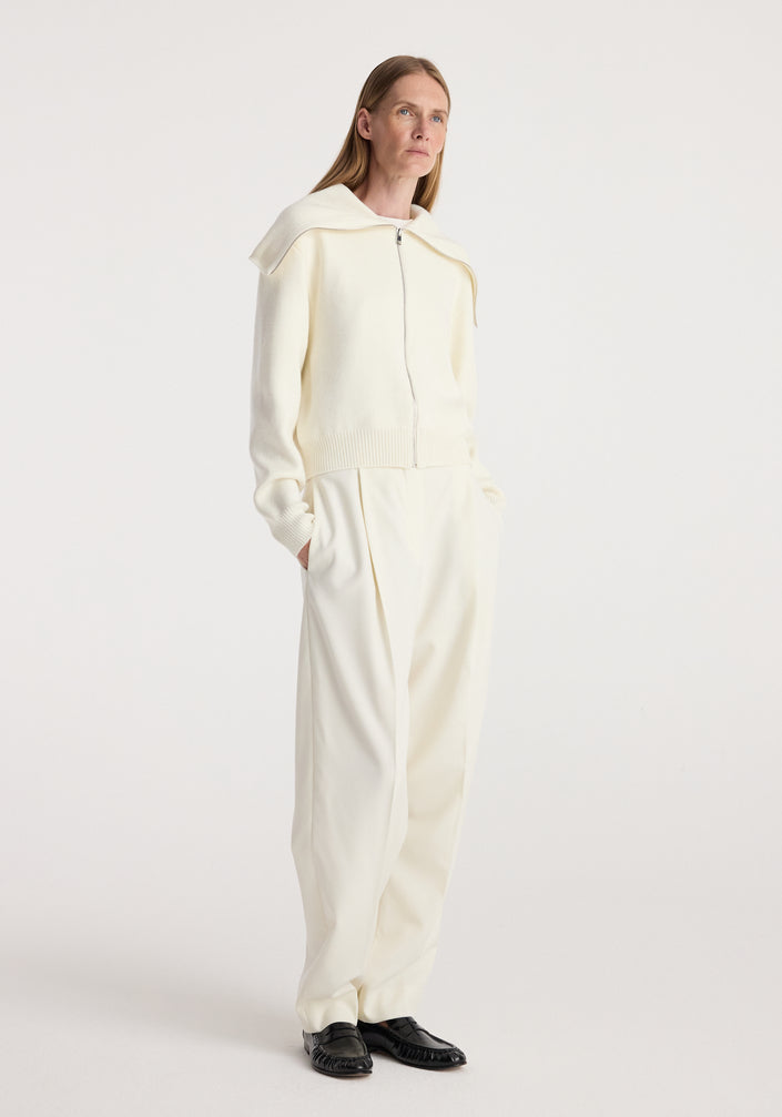 Woman wearing a cream Two way sailor zip cardigan | cream with long sleeves and a wide sailor collar, paired with matching cream wide-leg pants and black shoes, standing against a white background.