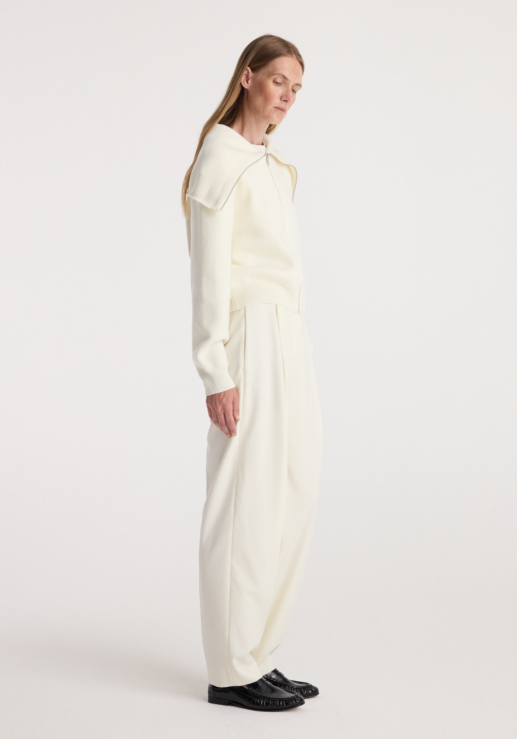 Woman wearing a cream long-sleeve Two way sailor zip cardigan | cream paired with loose cream pants and black loafers, standing in profile against a plain background.