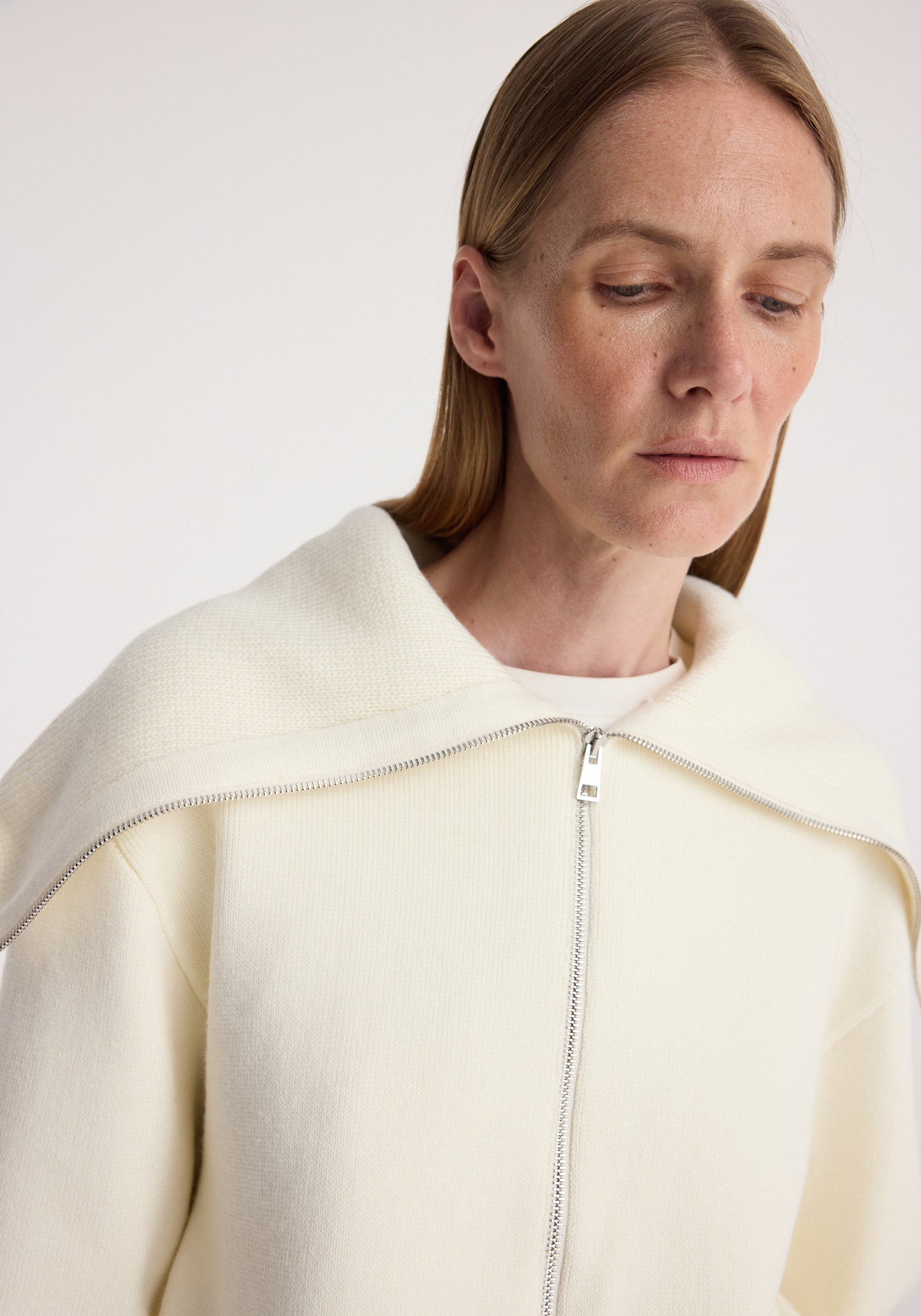 Close-up of a woman wearing a cream-colored Two way sailor zip cardigan | cream with a zipper detail and a wide sailor collar draped over the shoulders.