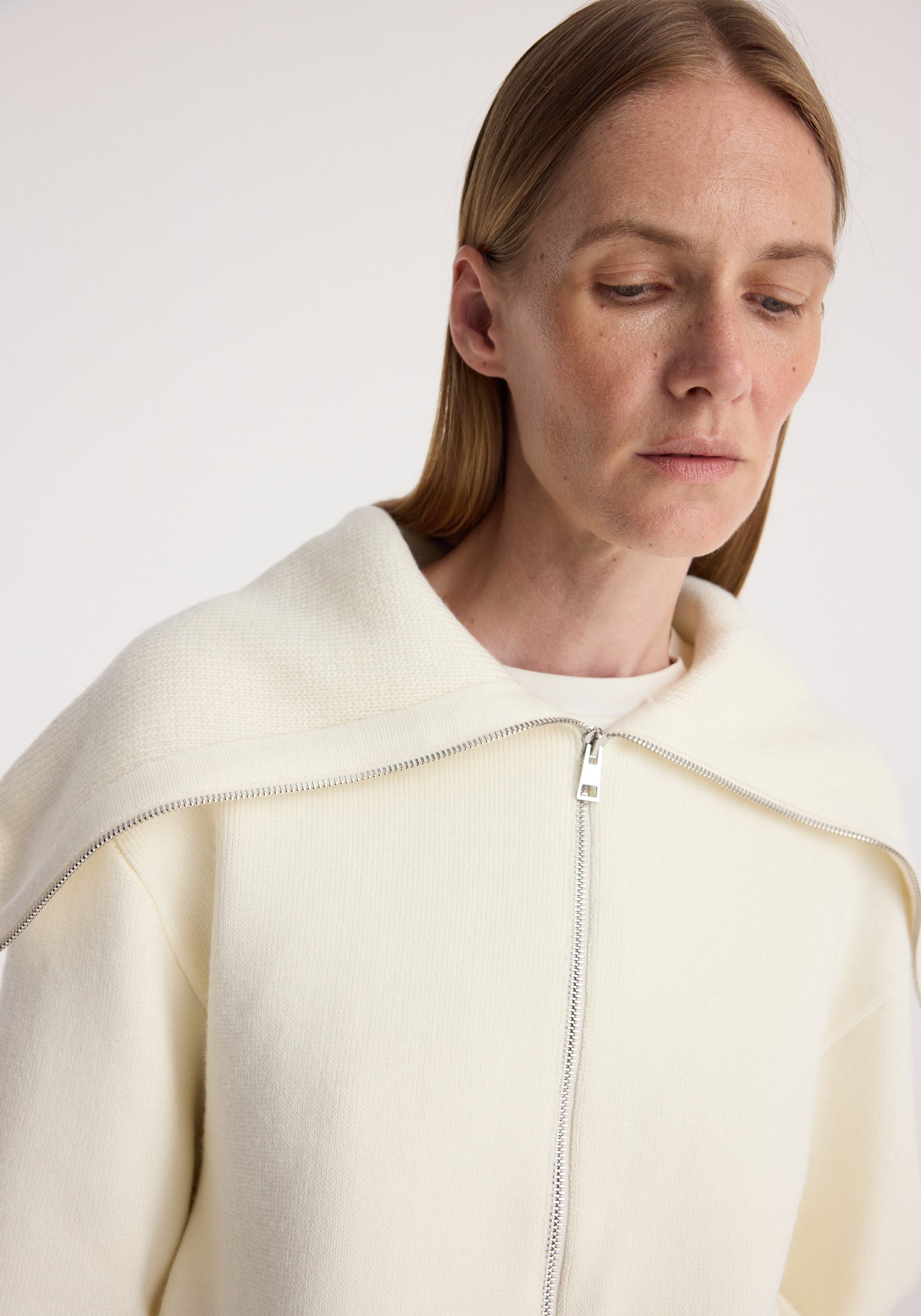 Close-up of a woman wearing a cream-colored Two way sailor zip cardigan | cream with a zipper detail and a wide sailor collar draped over the shoulders.