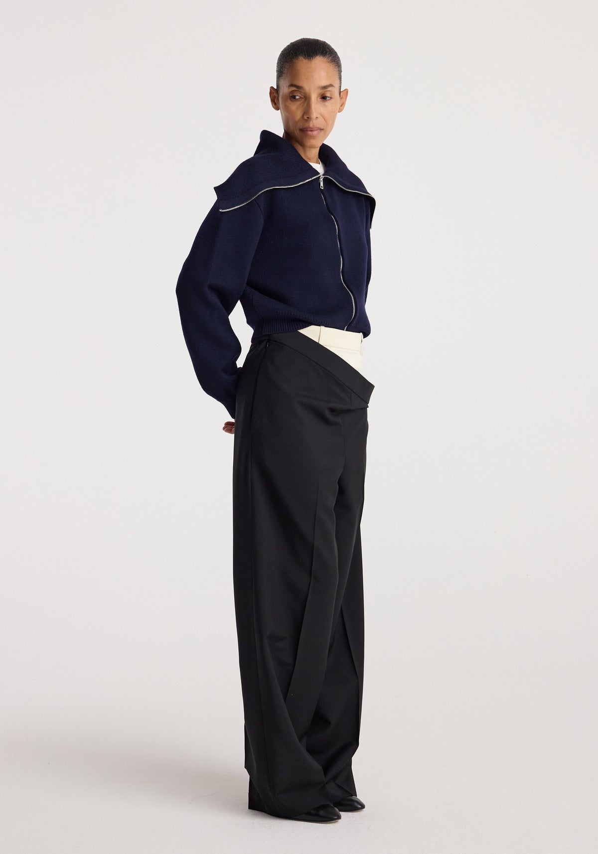 Woman wearing a navy zip-up cardigan with a sailor collar paired with high-waisted black wide-leg pants, styled in a minimalist fashion look, featuring the Two way sailor zip cardigan | navy.