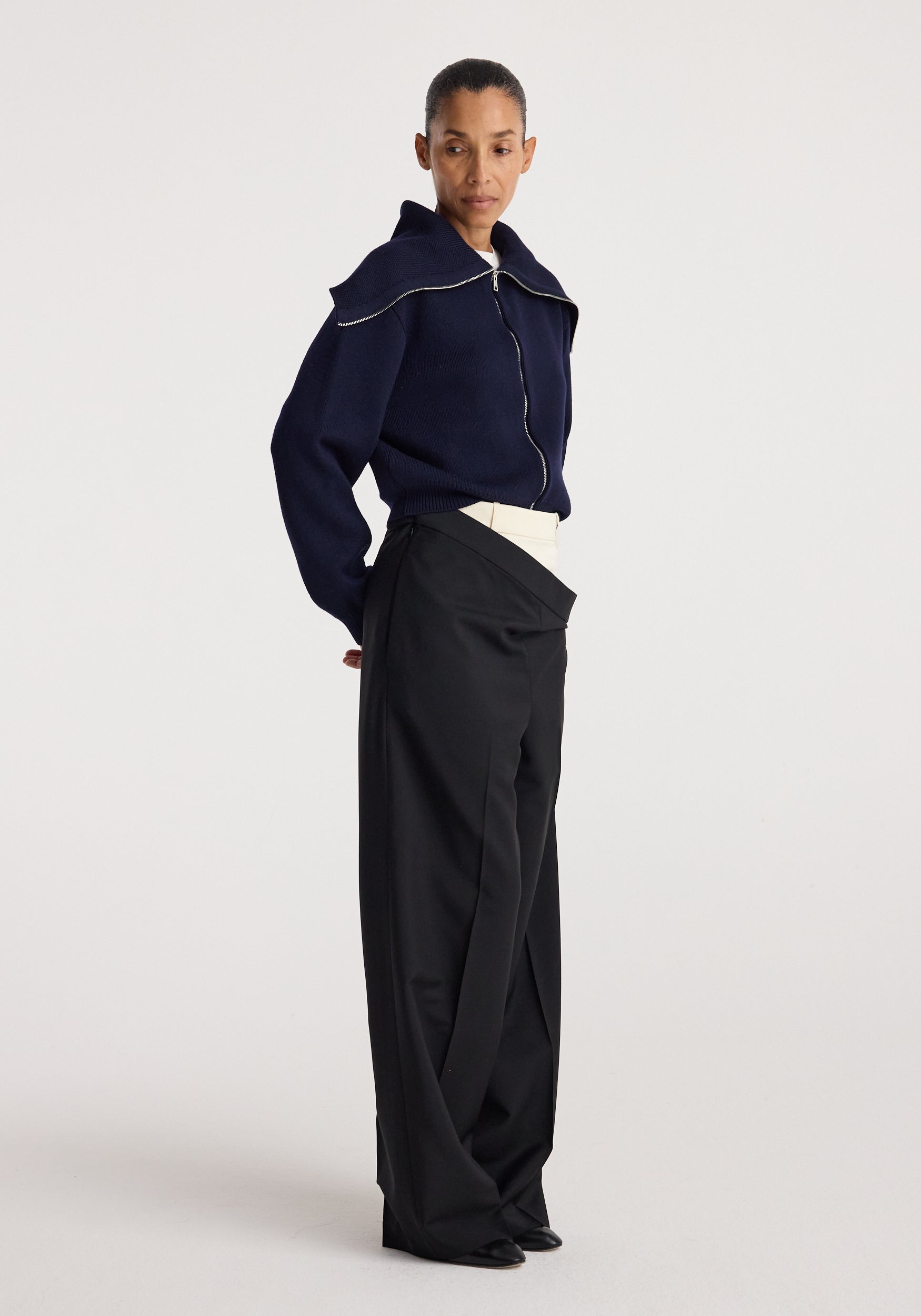 Woman wearing a navy zip-up cardigan with a sailor collar paired with high-waisted black wide-leg pants, styled in a minimalist fashion look, featuring the Two way sailor zip cardigan | navy.