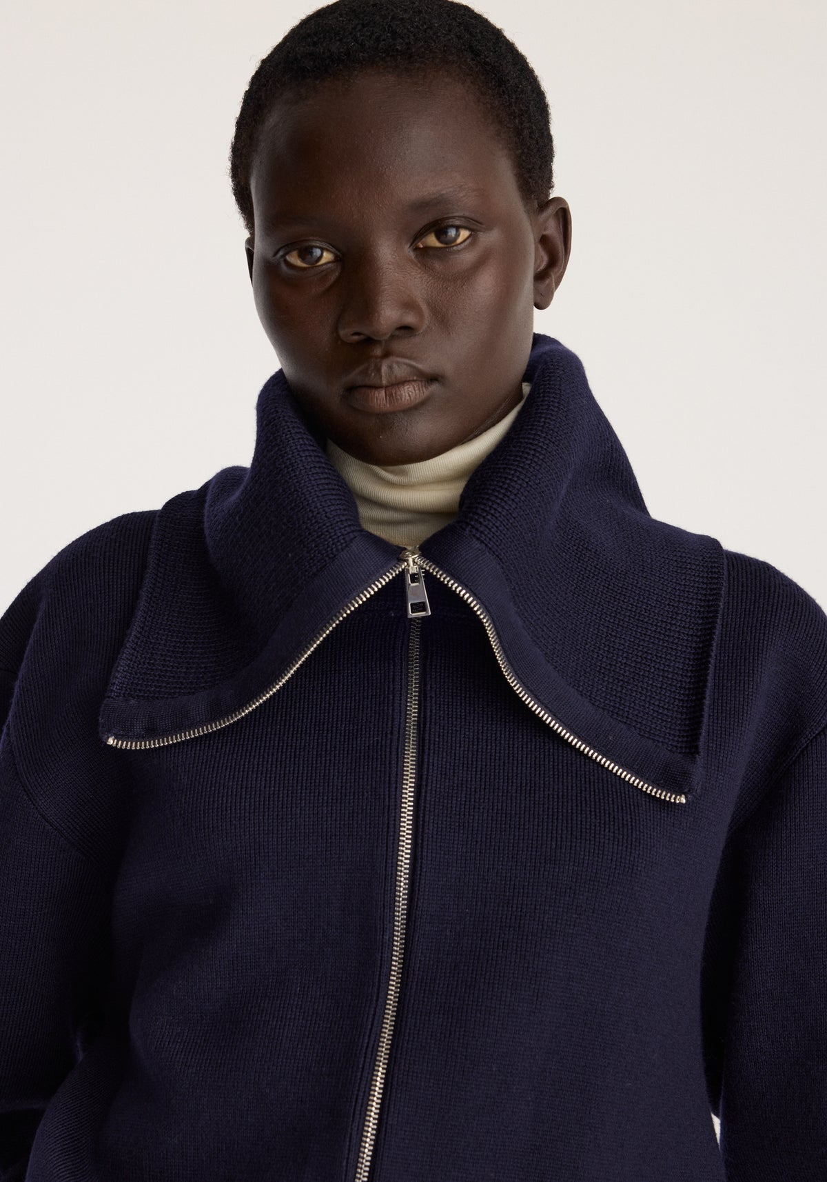 Reversible sailor zip cardigan | navy worn by a model with a high collar and curved front zipper detail in a close up portrait pose
