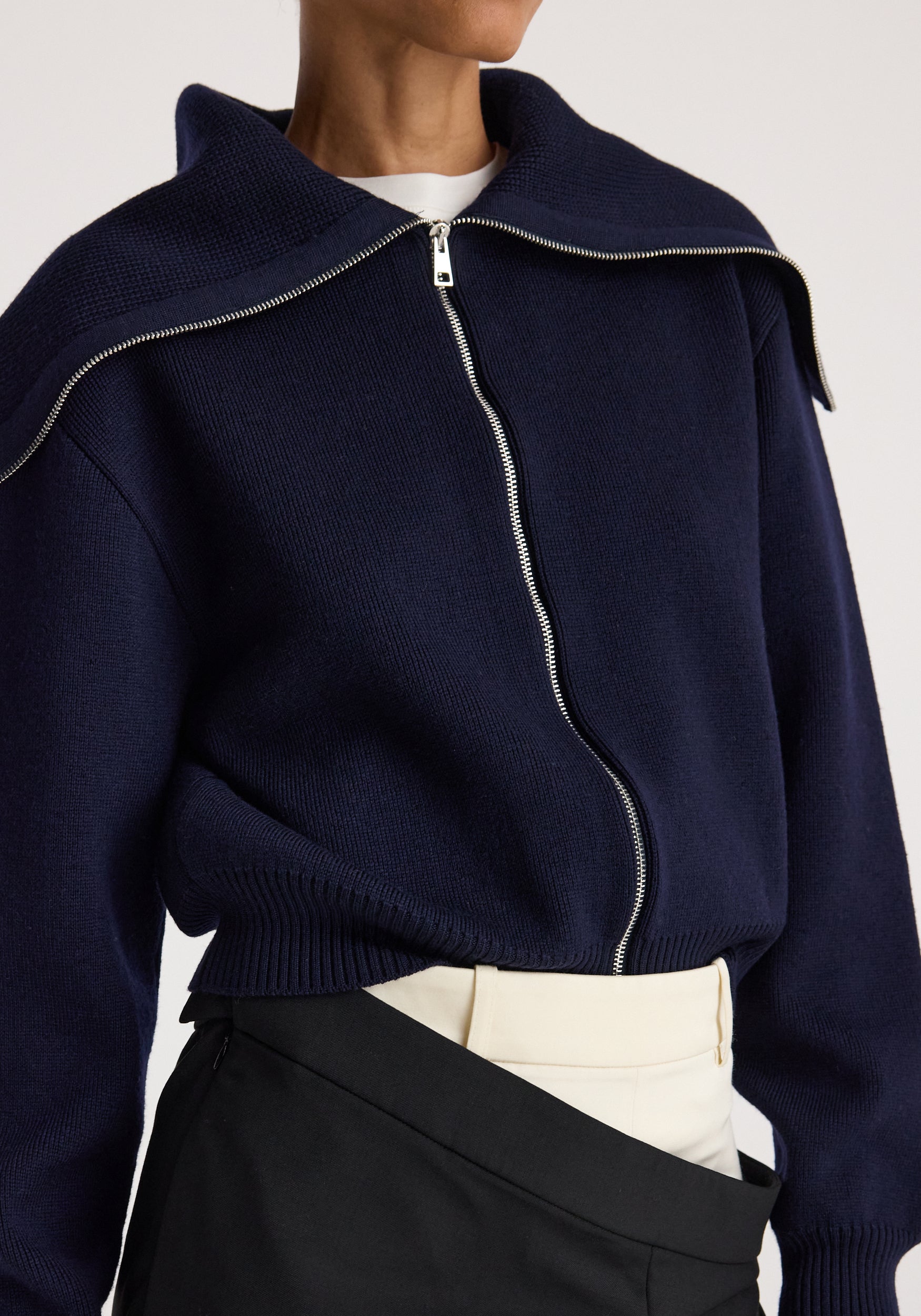 Close-up of a person wearing a navy blue Two way sailor zip cardigan | navy with a silver zipper, styled with light and dark layered bottoms.