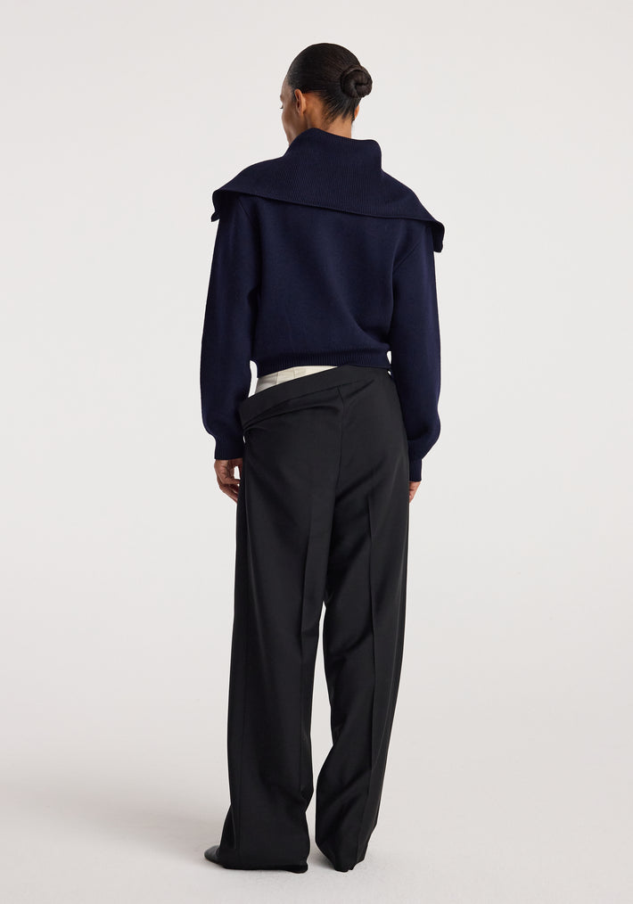 Woman seen from behind wearing a navy blue Two way sailor zip cardigan | navy with a wide collar paired with black wide-leg trousers against a plain background.