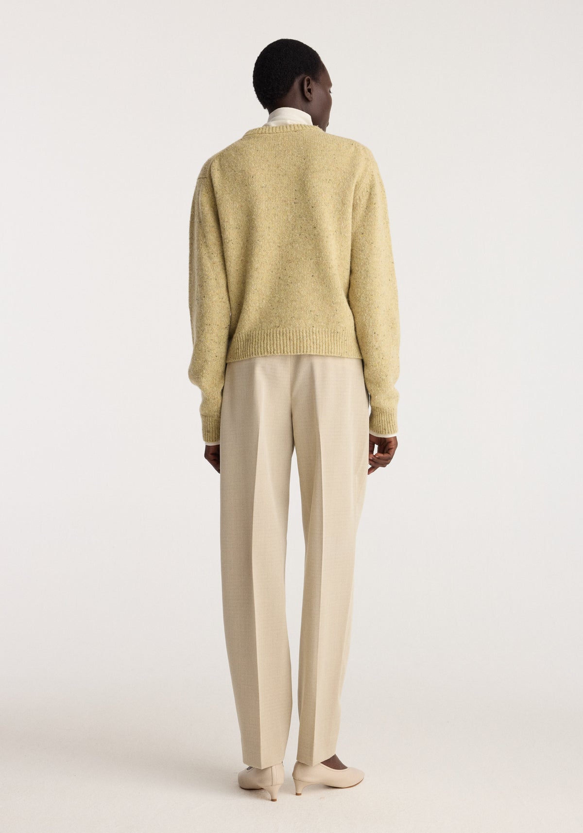 Back view of a model wearing the Fitted mouliné crewneck | butter mouliné sweater with cream trousers and neutral shoes in a studio setting