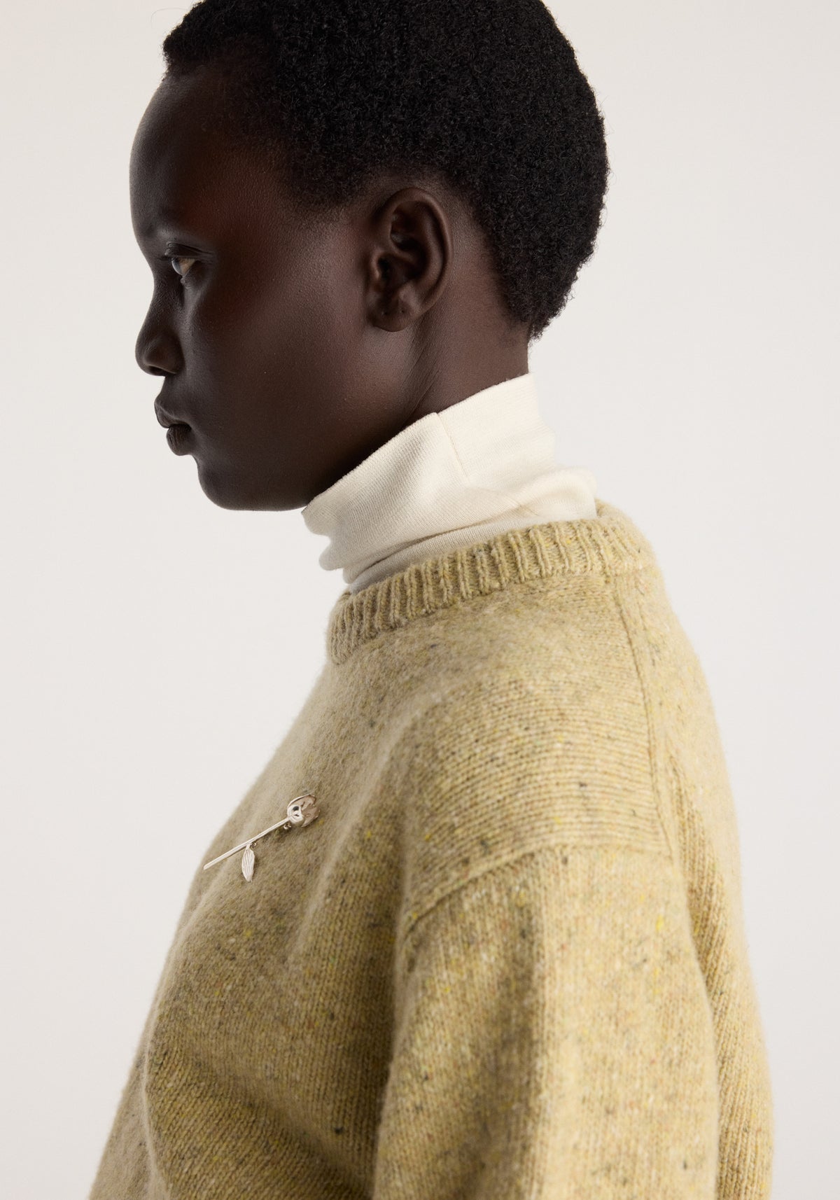 Profile view of a model wearing the Fitted mouliné crewneck | butter mouliné in soft yellow knit with a high white collar and brooch detail.