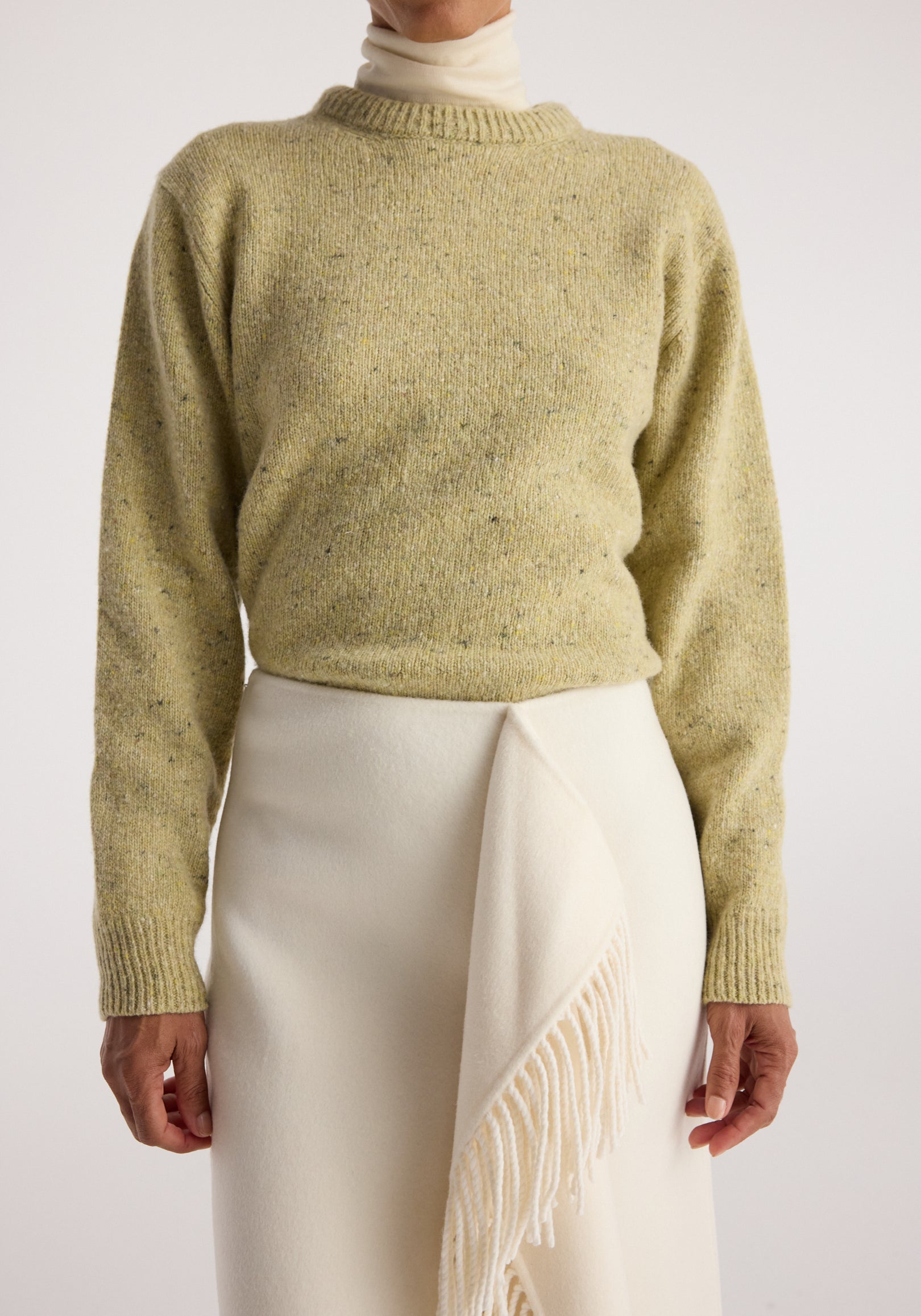 Close-up of a person wearing a textured light yellow knit sweater over a cream turtleneck, paired with a white skirt featuring a fringed detail, showcasing the Fitted mouliné crewneck | butter mouliné.
