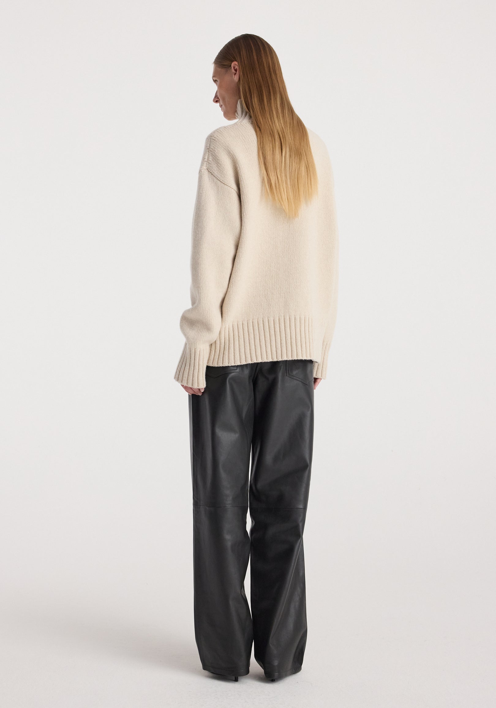 Model wearing a Wool-cashmere turtleneck | oat in a relaxed fit, shown from the back paired with black wide-leg pants against a plain white background.
