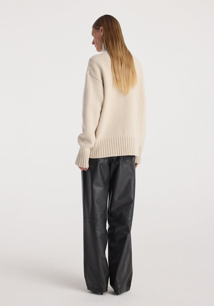 Model wearing a Wool-cashmere turtleneck | oat in a relaxed fit, shown from the back paired with black wide-leg pants against a plain white background.