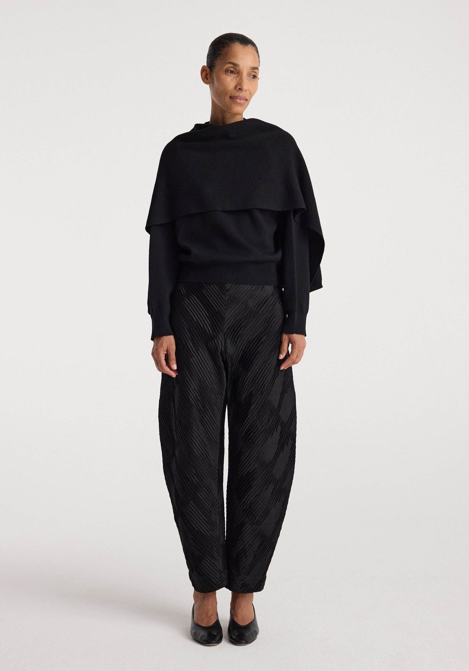Woman wearing a black layered top with long sleeves and textured black pants, styled with black shoes, showcasing the Cape jumper | black.