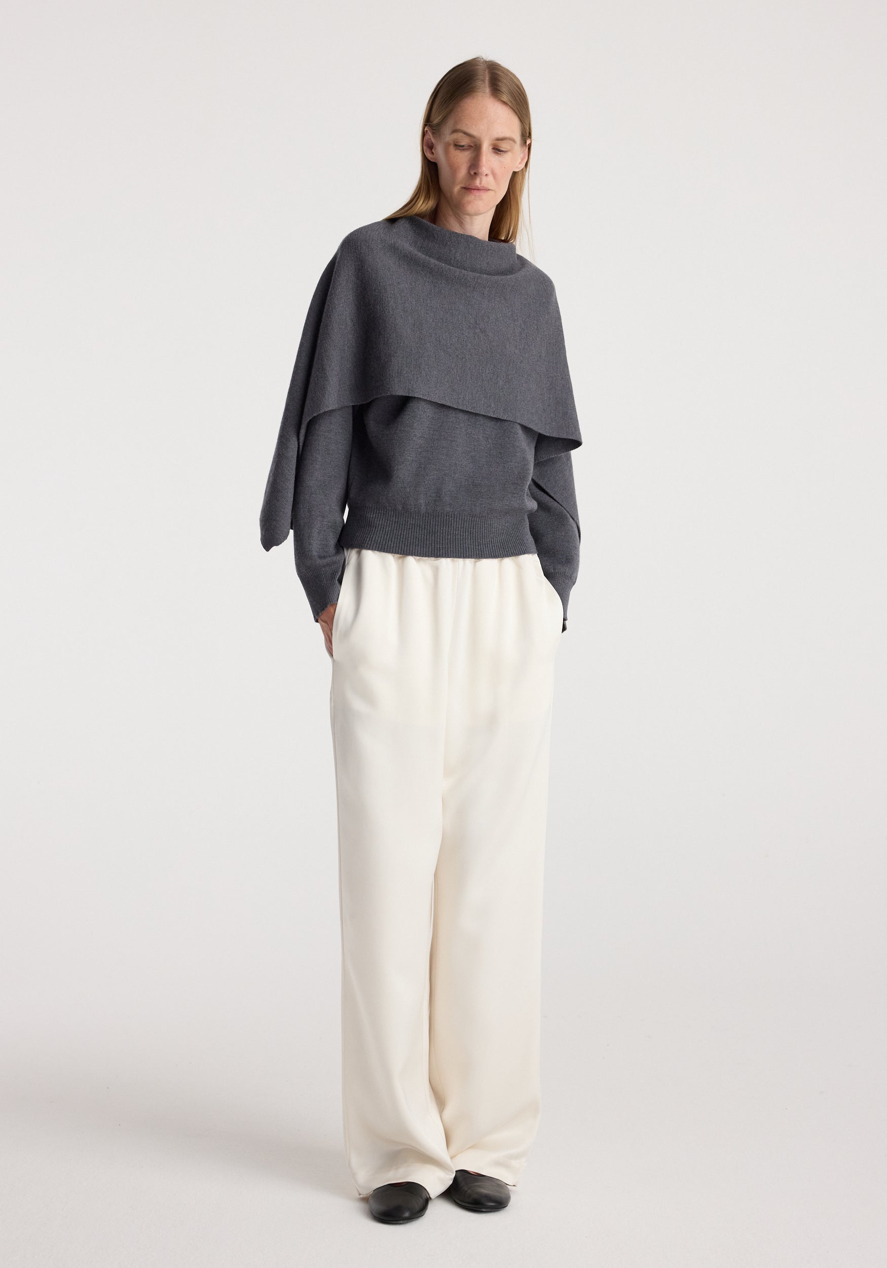 Woman wearing a dark grey melange layered sweater with a loose fit over cream wide-leg trousers and black shoes, featuring the Cape jumper | dark grey melange.