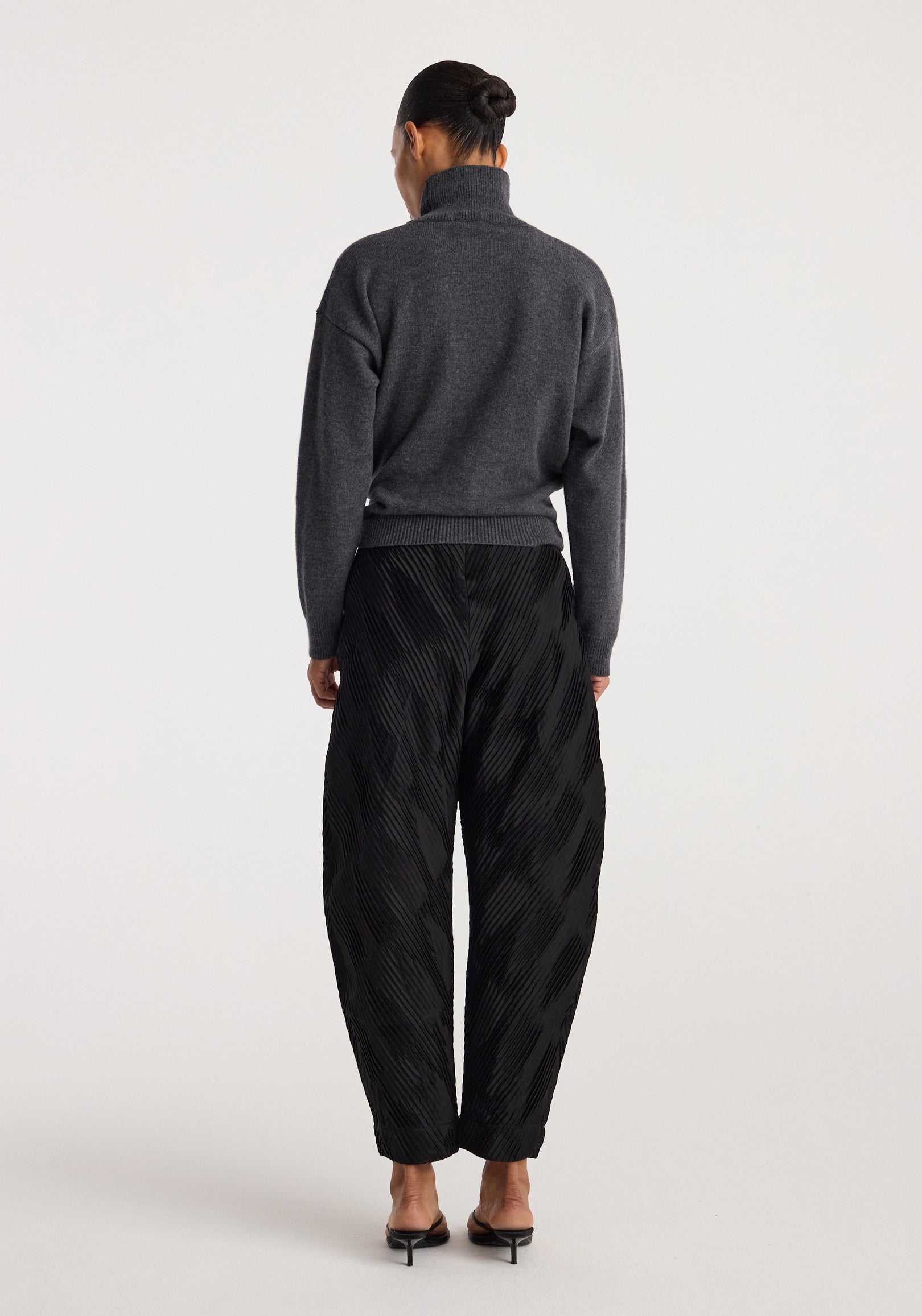 Back view of a person wearing a Sculptural turtleneck | dark grey melange with long sleeves paired with black textured wide-leg pants and black heeled sandals.