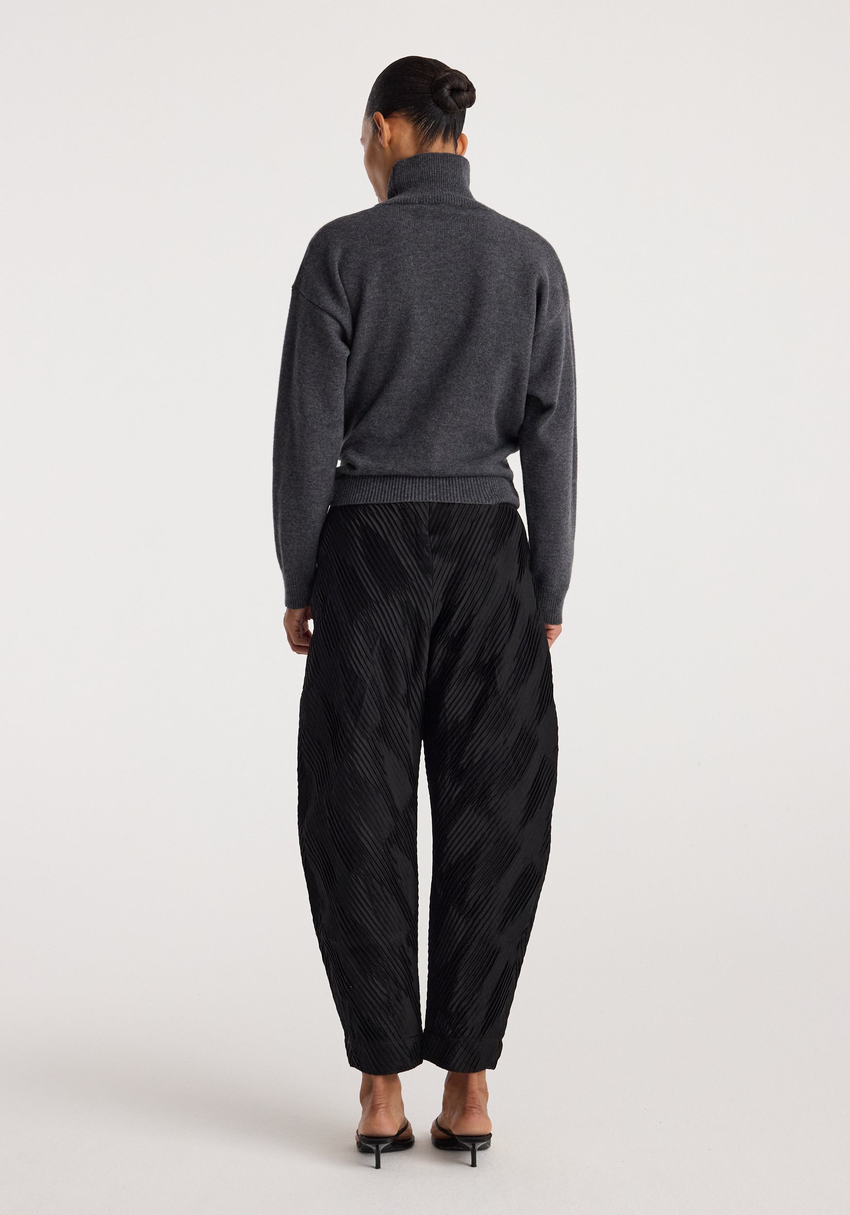 Back view of a person wearing a Sculptural turtleneck | dark grey melange with long sleeves paired with black textured wide-leg pants and black heeled sandals.
