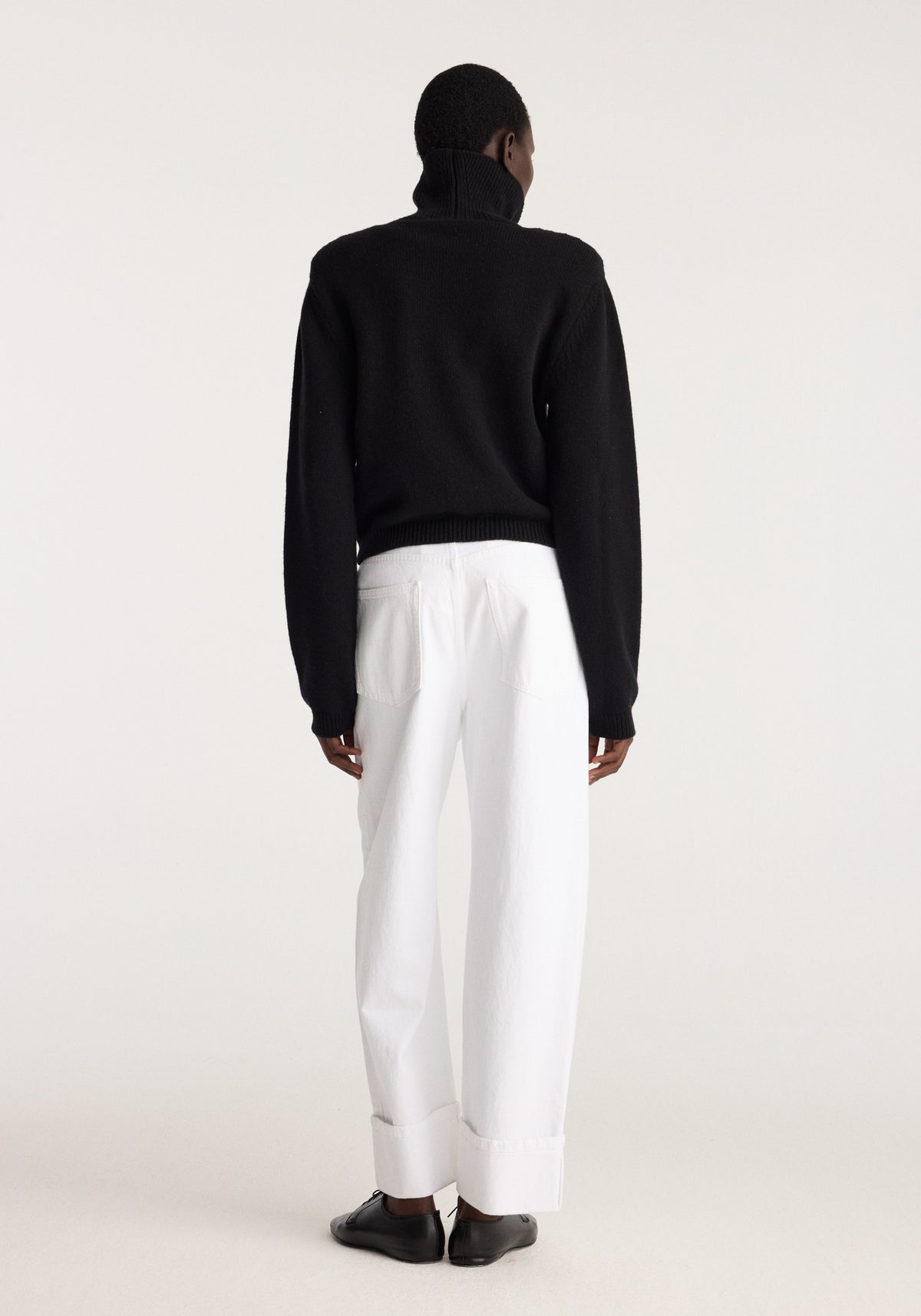 Statement shoulder turtleneck | black shown from the back on a model with a high neck long sleeves and ribbed hem styled with white trousers and black shoes