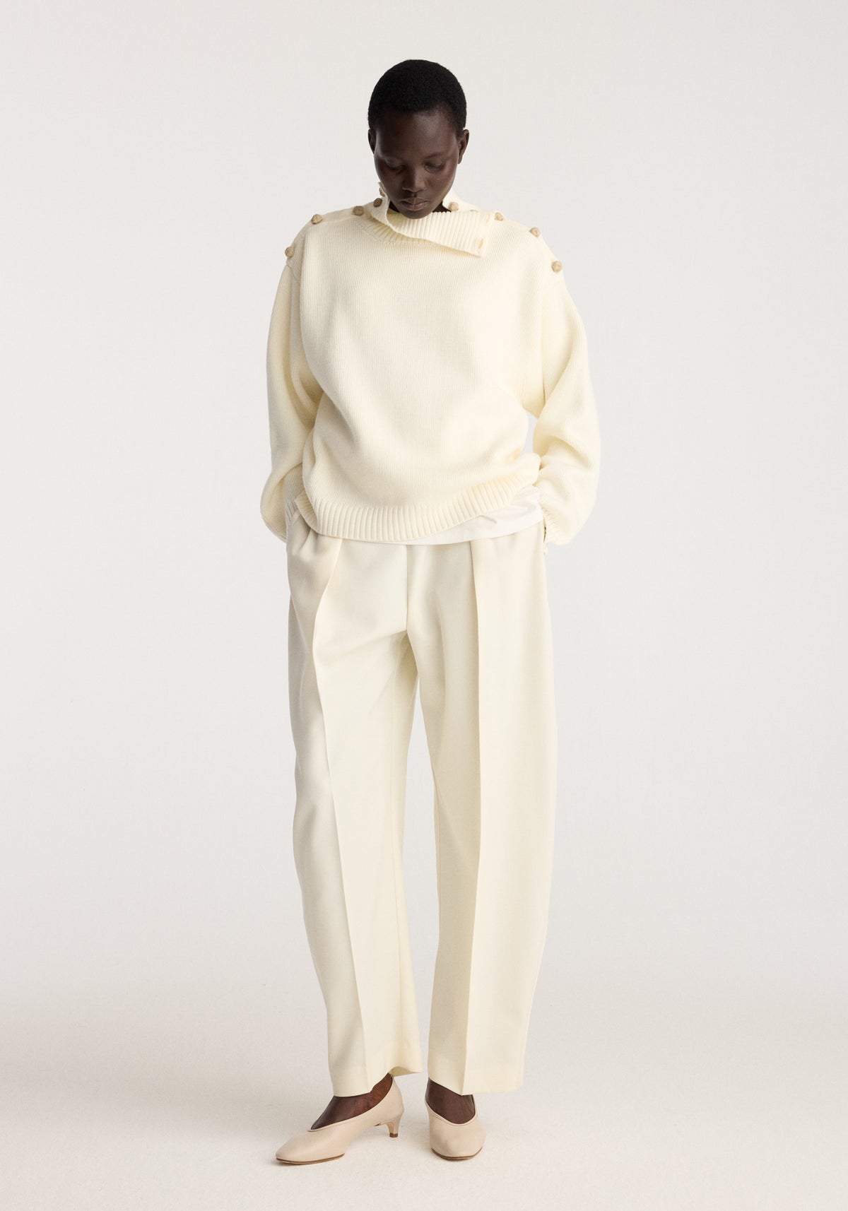 Uneven sailor polo | cream worn with matching cream trousers and neutral shoes by a model in a softly lit studio setting