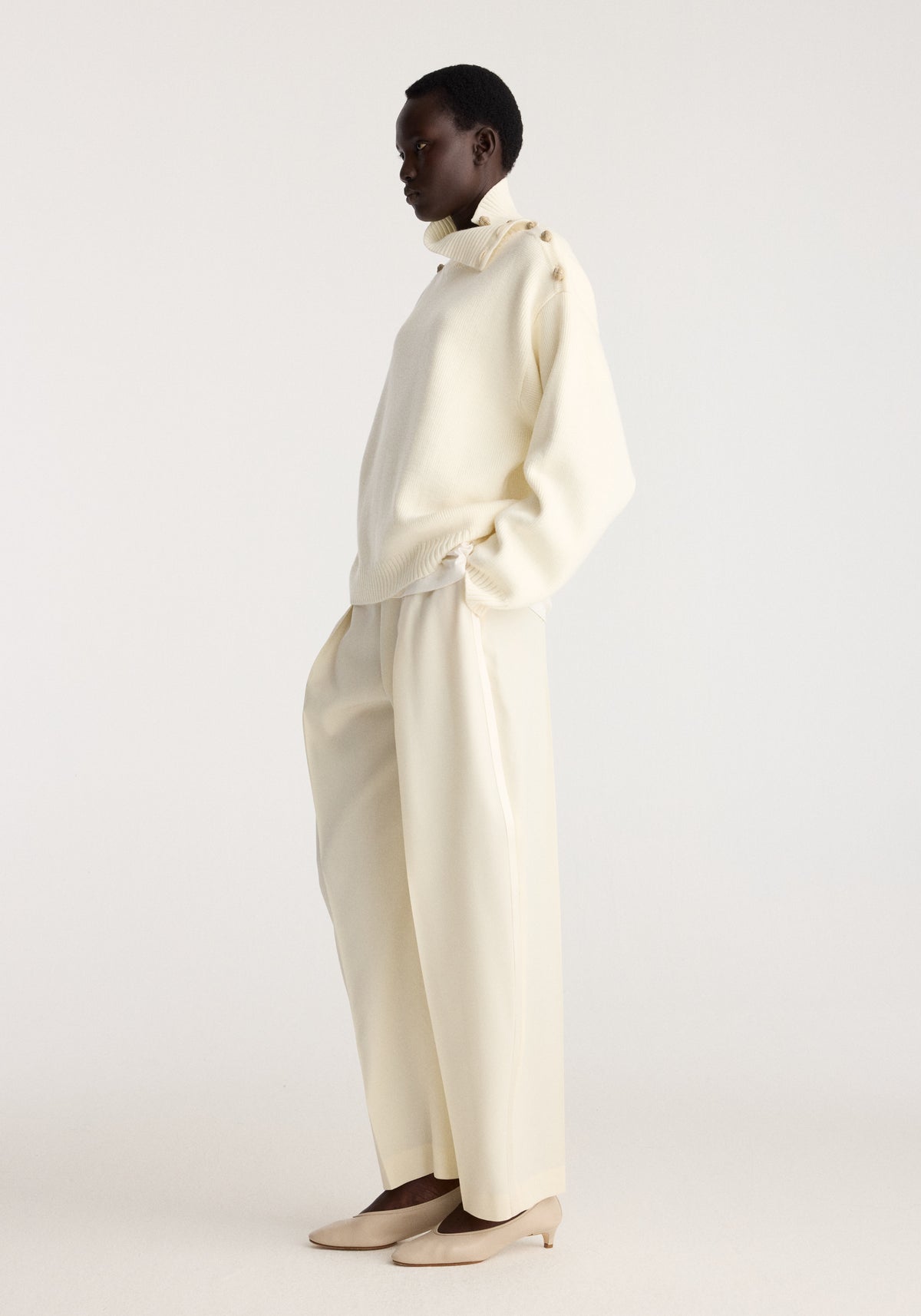 Model in profile wearing the Uneven sailor polo | cream with a high collar and relaxed fit styled with matching cream trousers and pointed flats