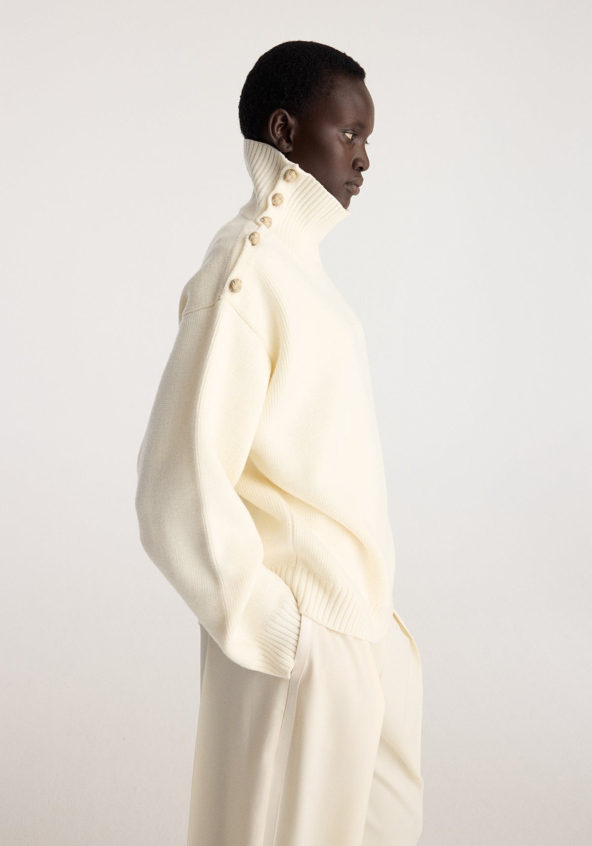 Uneven sailor polo | cream shown in side profile on a model, featuring a high ribbed collar with buttons and relaxed cream knit styling