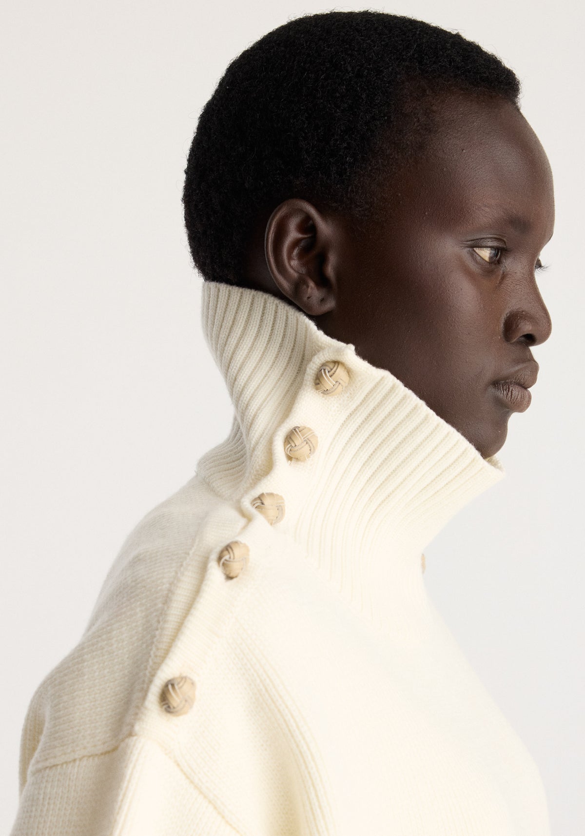 Uneven sailor polo | cream worn by a model in profile featuring a high ribbed collar and button details
