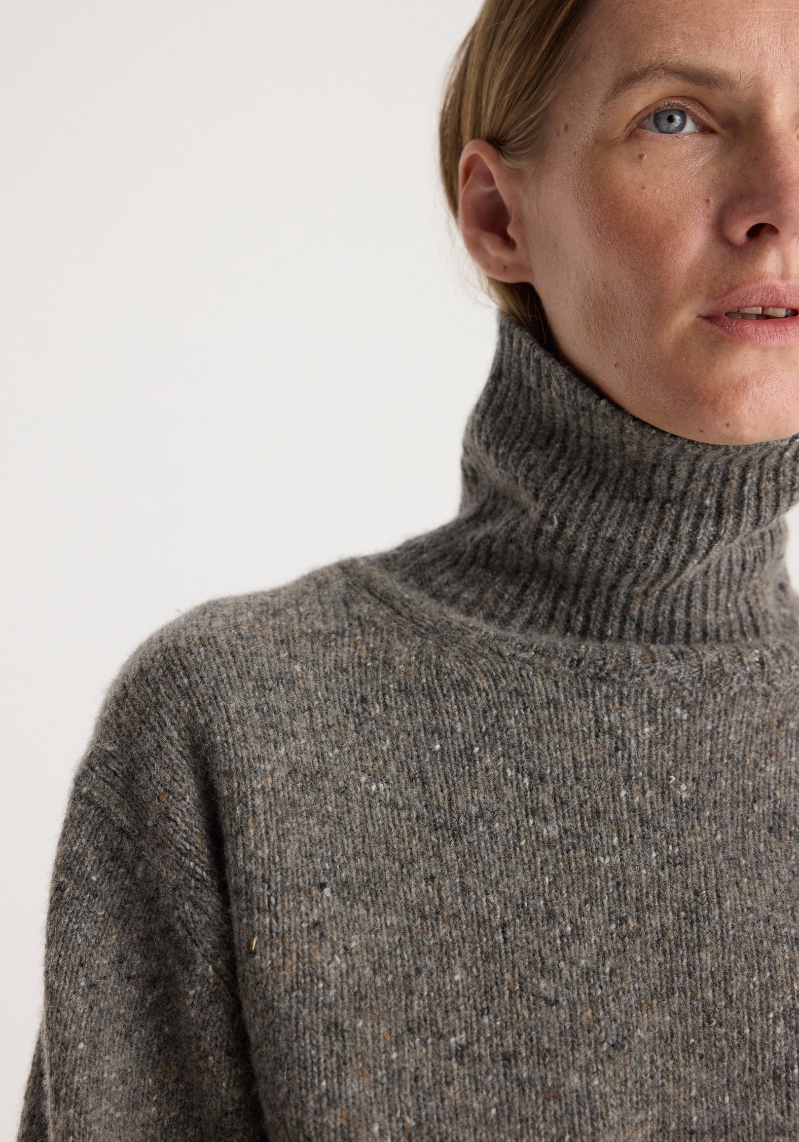 Close-up of a person wearing a cozy, textured grey knit high-neck sweater showcasing the soft fabric and ribbed collar of the Mouliné turtleneck | grey mouliné.