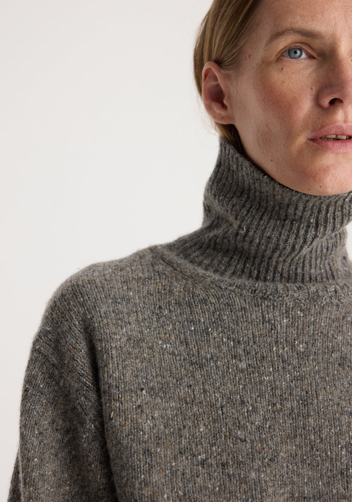 Close-up of a person wearing a cozy, textured grey knit high-neck sweater showcasing the soft fabric and ribbed collar of the Mouliné turtleneck | grey mouliné.