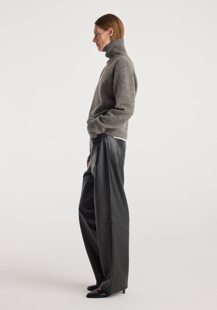 Woman wearing a grey textured Mouliné turtleneck | grey mouliné sweater paired with wide-leg black leather pants and black pointed-toe shoes, standing in profile against a plain background.