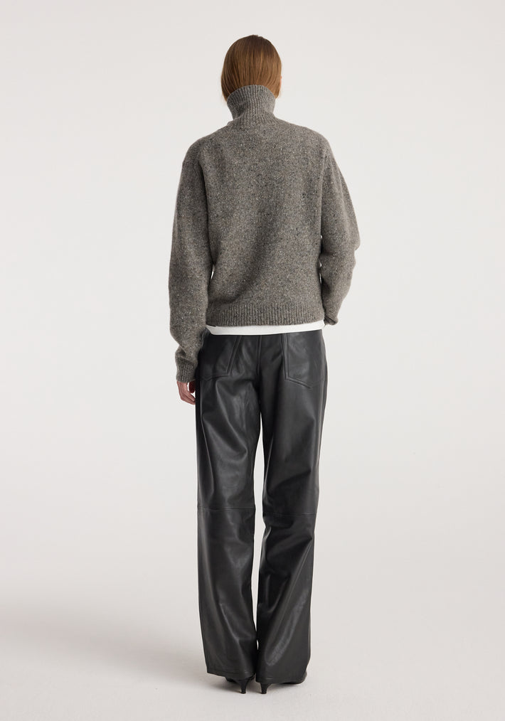 Rear view of a person wearing a grey Mouliné turtleneck | grey mouliné sweater with a high neck and long sleeves paired with black wide-leg leather pants against a plain white background.