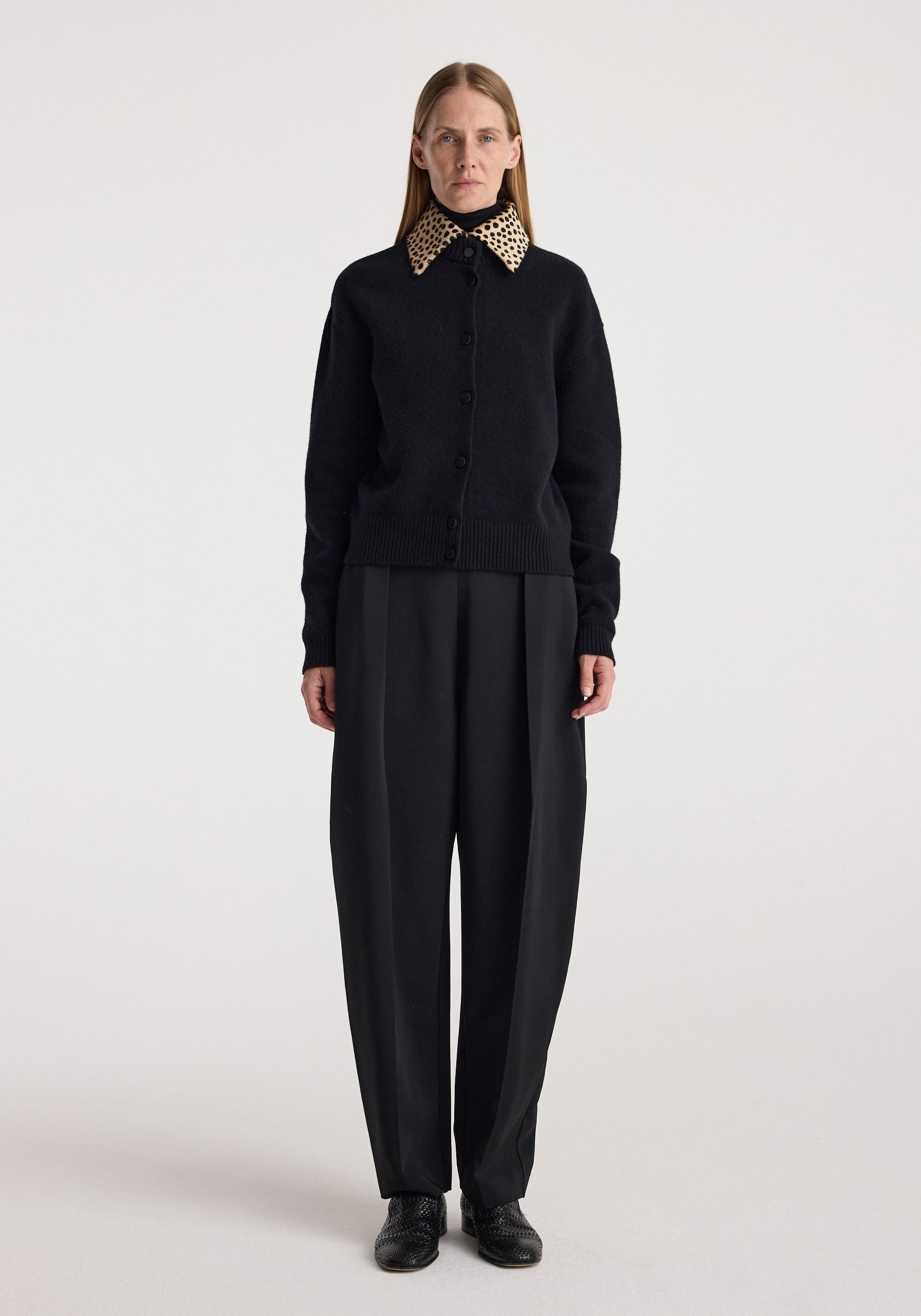 Woman wearing a black button-up sweater with a cheetah print collar, paired with loose black trousers and black shoes, modeling the Cheetah collar cardigan | black.