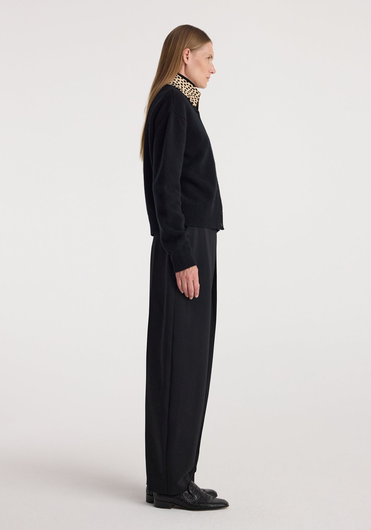 Side profile of a woman wearing a Cheetah collar cardigan | black, paired with black wide-leg pants and black shoes against a plain light background.