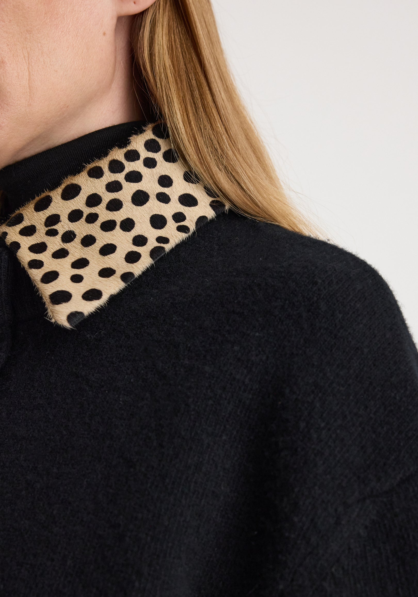 Close-up of a black sweater featuring a cheetah collar cardigan | black with a spotted animal print collar detail on a person with long blonde hair.