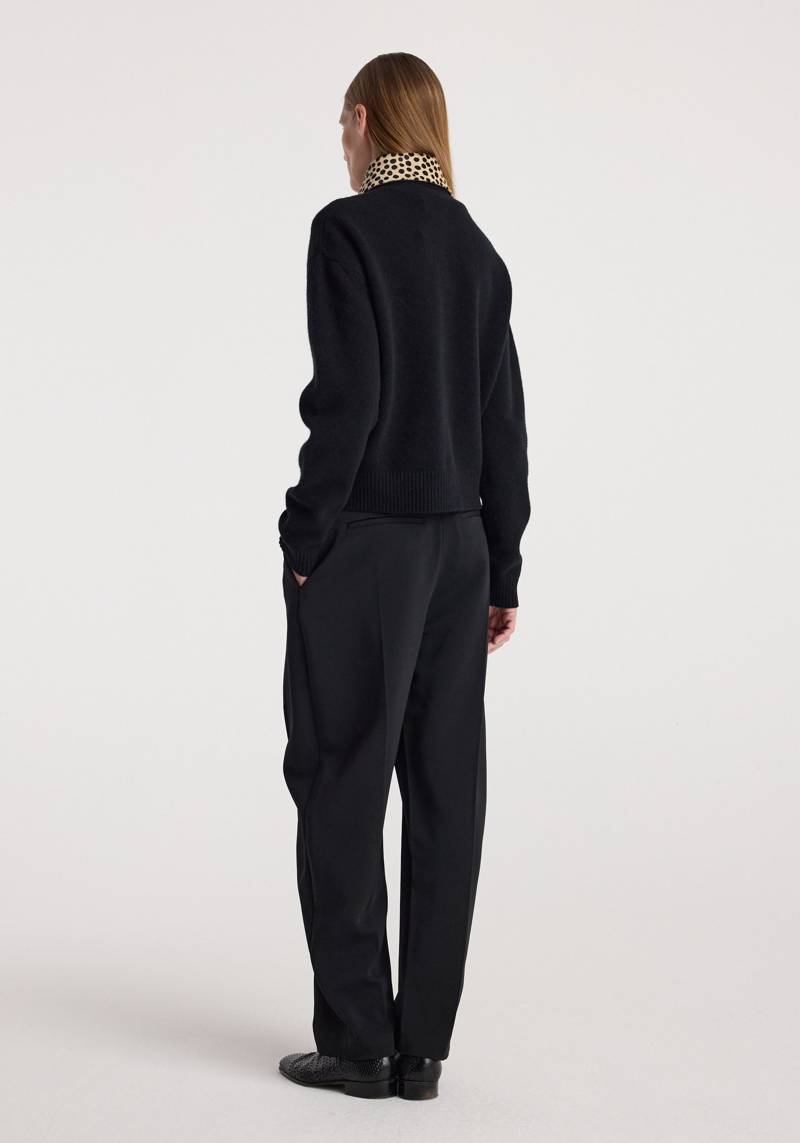 Woman seen from behind wearing cheetah collar cardigan | black with matching black pants and shoes against a plain light background.