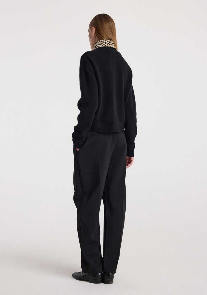 Woman seen from behind wearing cheetah collar cardigan | black with matching black pants and shoes against a plain light background.