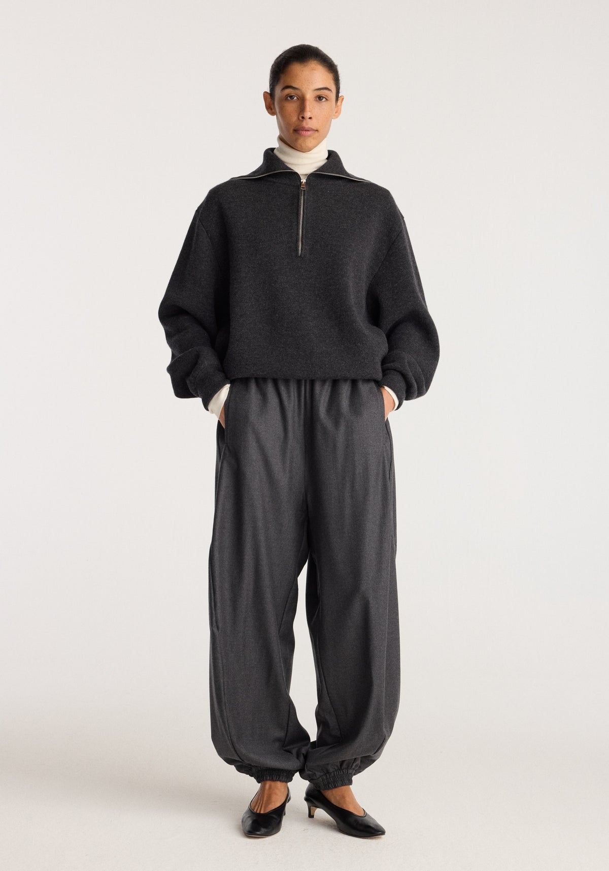 Reversible zipped turtleneck | charcoal worn by a model with wide charcoal trousers and black shoes, showing the quarter zip and high neck.